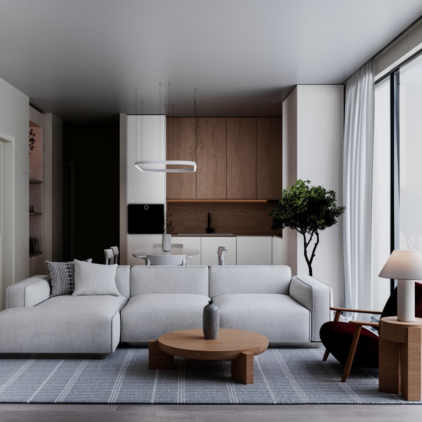 A modern, minimalist open-concept living and kitchen area. The living room features a white sectional sofa and a round wooden coffee table on a grey and white striped rug. The kitchen has a mix of white and light wood cabinetry with a round dining table.