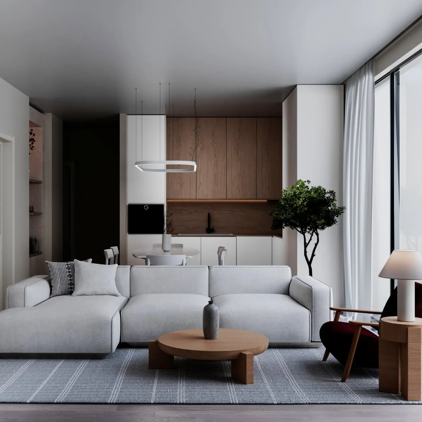 A modern, minimalist open-concept living and kitchen area. The living room features a white sectional sofa and a round wooden coffee table on a grey and white striped rug. The kitchen has a mix of white and light wood cabinetry with a round dining table.