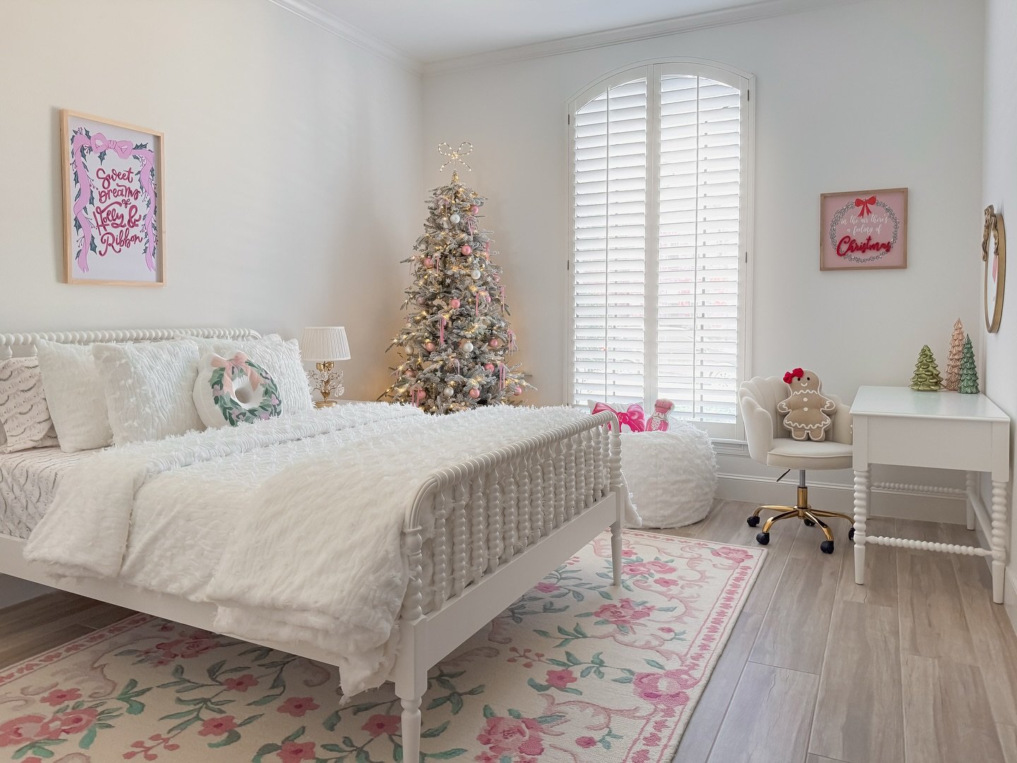 A festive teen girl's bedroom decorated for Christmas with a white and pink color scheme, featuring a decorated tree, a white spindle bed, and holiday art.