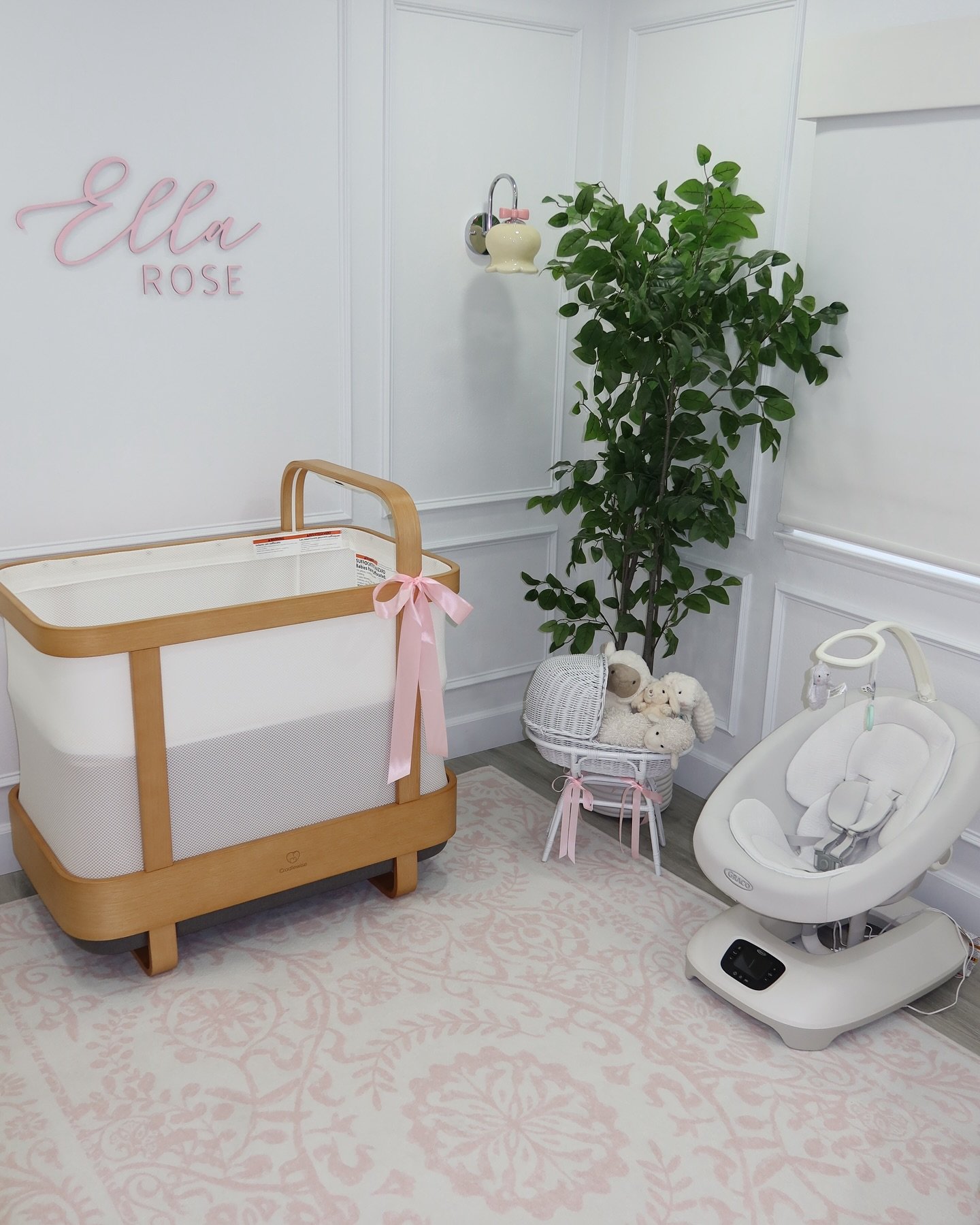 A soft and sweet nursery with a modern bassinet, a pink and white rug, and a custom name sign on the wall
