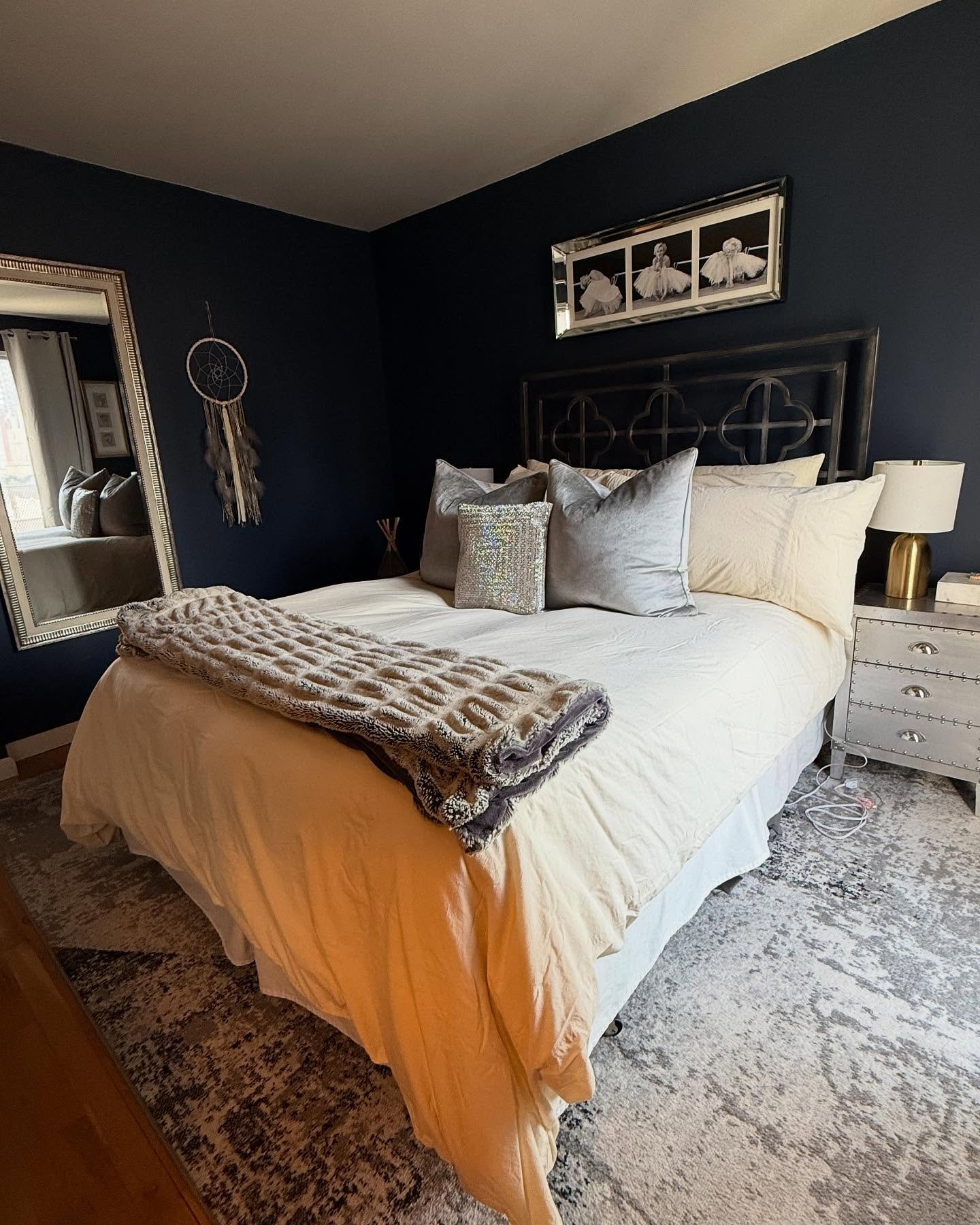 A large, abstract area rug with a faded pattern in shades of light gray and beige is placed under a bed in a bedroom with dark navy blue walls.
