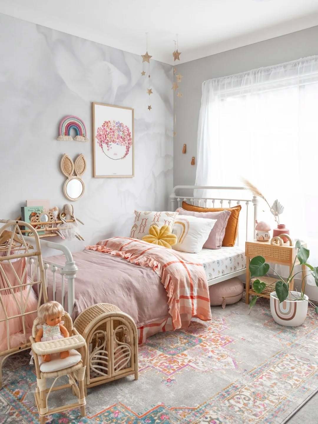 A whimsical and bohemian girl's bedroom with a pink duvet, colorful patterned pillows, a watercolor floral portrait, and rattan furniture.