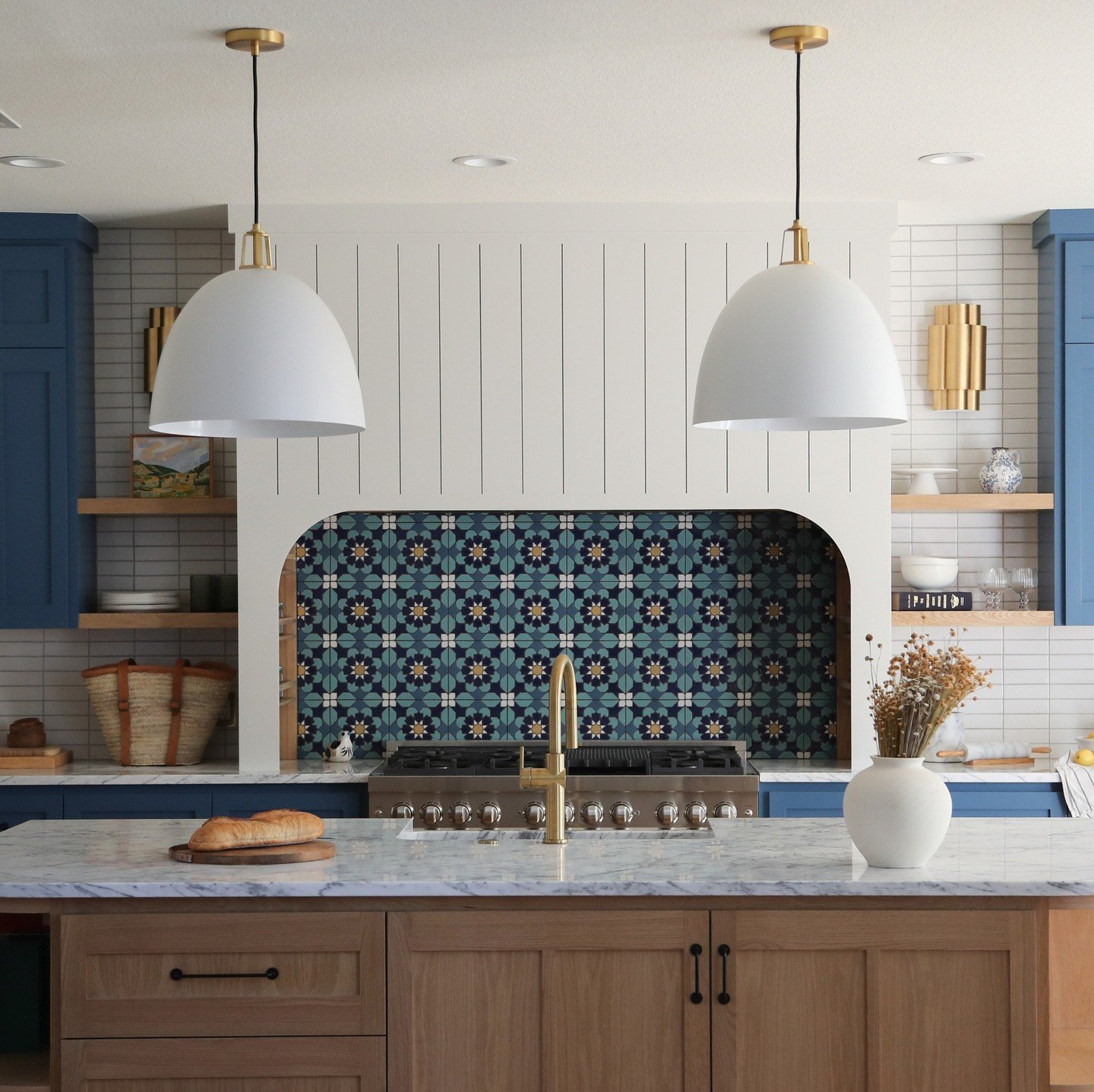A kitchen featuring a vibrant, Mediterranean-style tile backsplash with a floral and geometric pattern in shades of blue and white, set against a backdrop of subway tiles and blue cabinetry.
