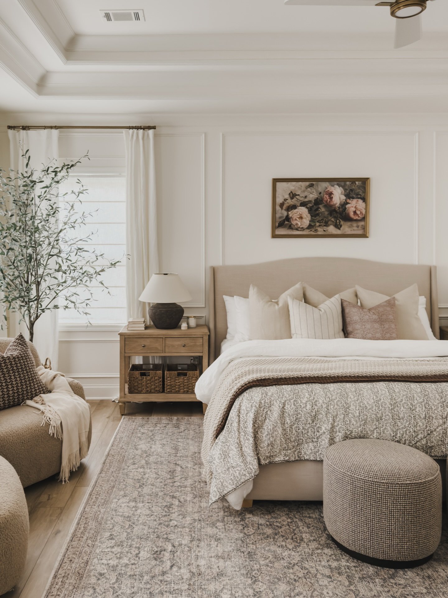 A large, patterned area rug in muted tones of gray and beige is placed under a bed with a beige headboard and a patterned comforter.