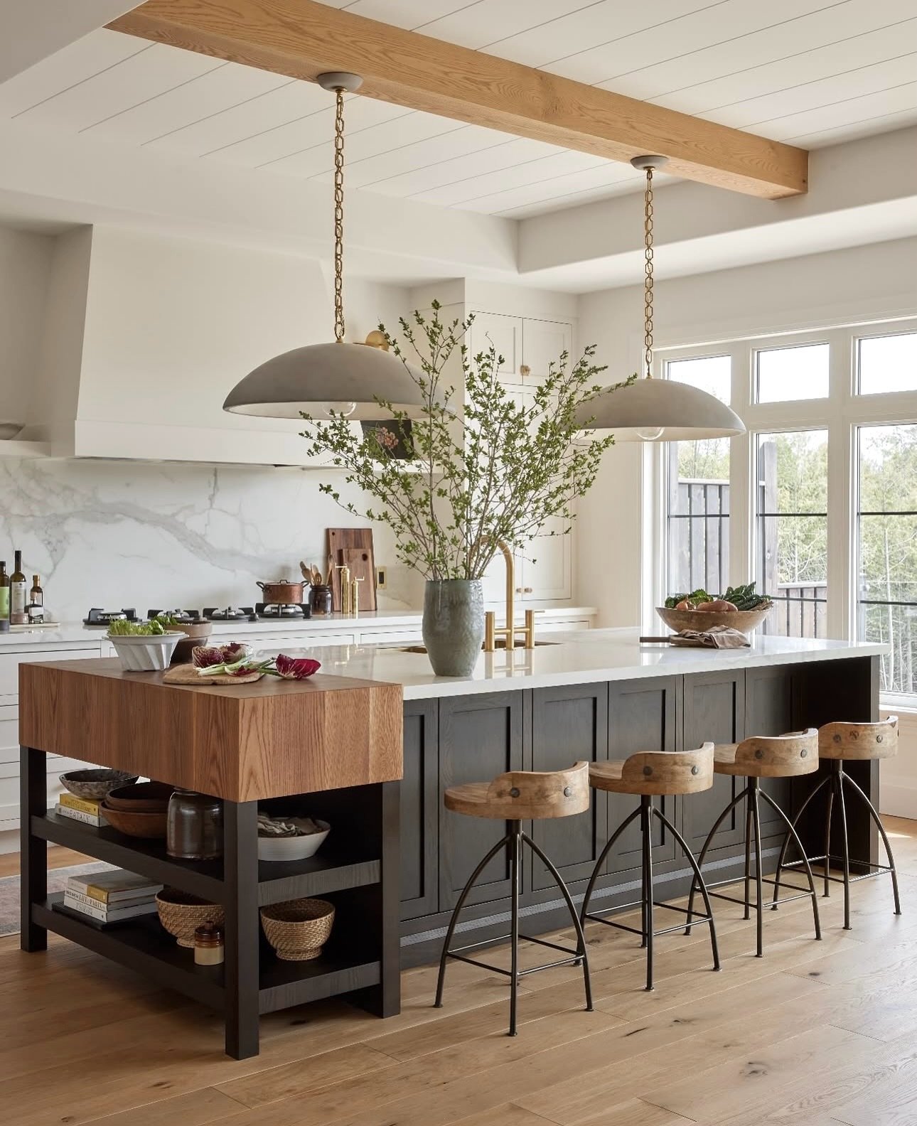 A large kitchen island with a dark gray base and a white countertop, featuring a built-in butcher block and industrial-style bar stools.
