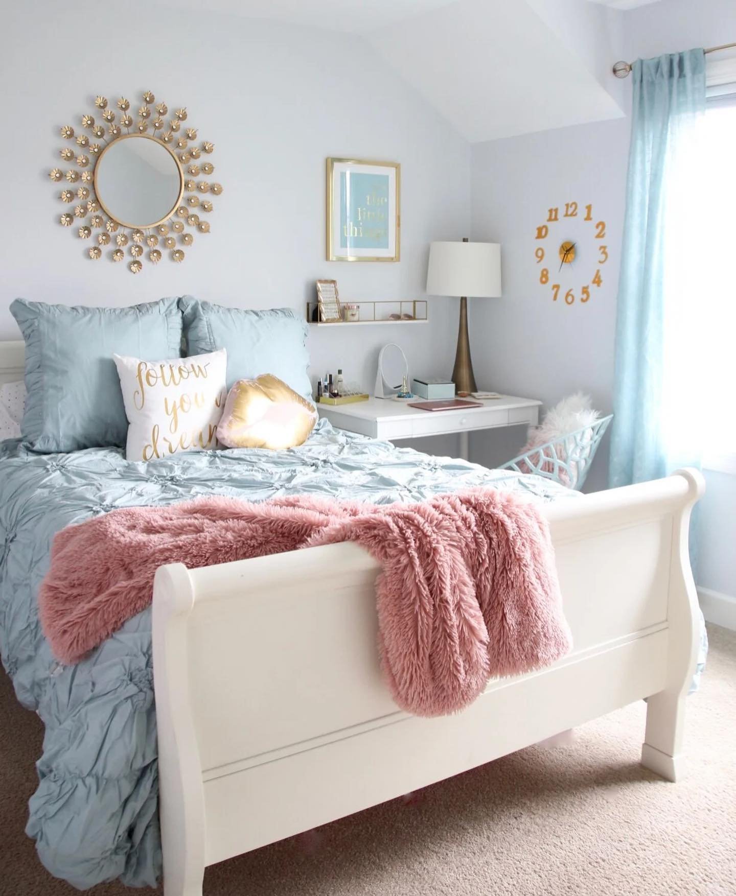 A cozy teen girl's bedroom with a light blue and pink color scheme, featuring a plush bed and a gold sunburst mirror.