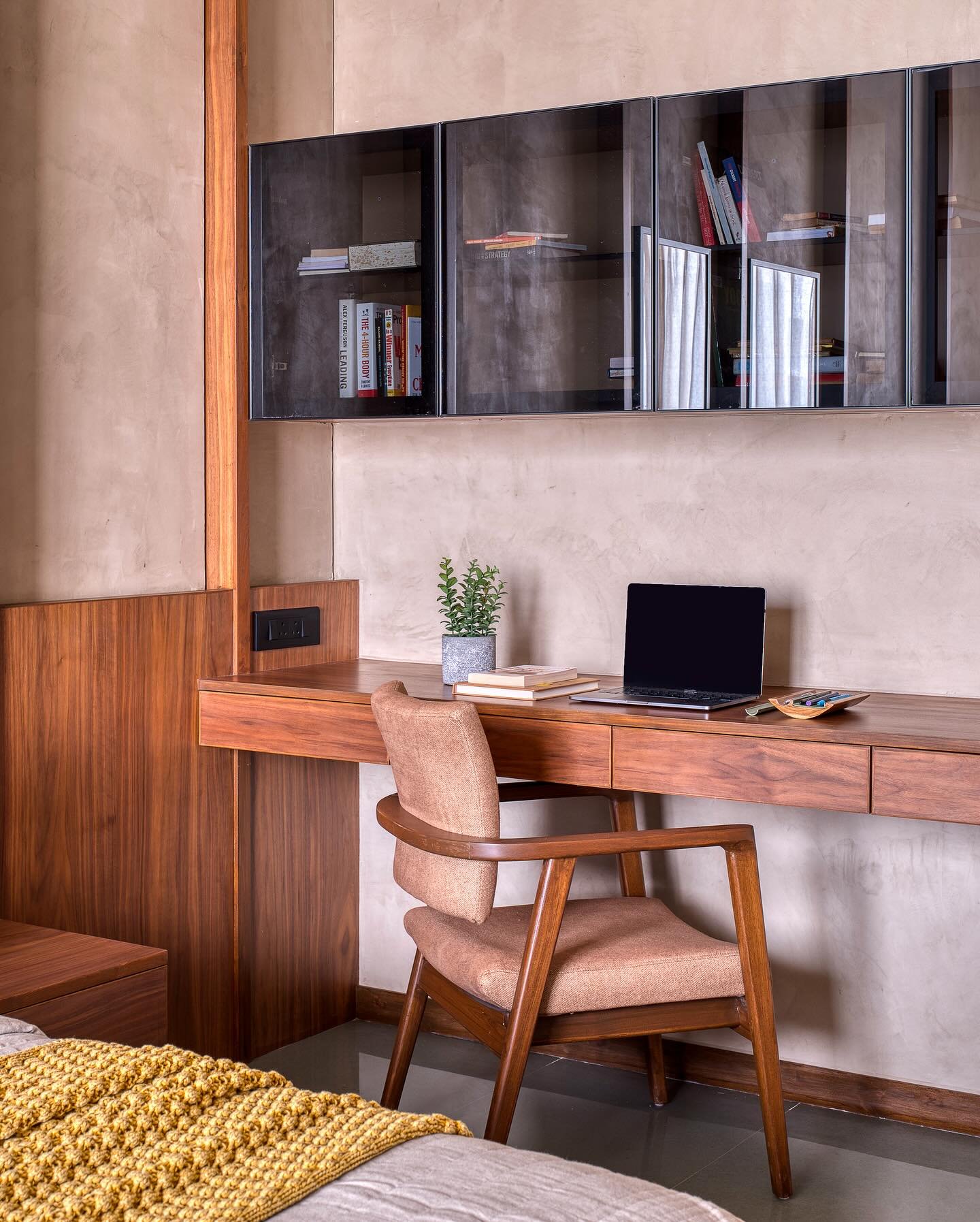A contemporary integrated wooden study desk featuring a floating design and two drawers, complemented by a matching chair and dark glass cabinets.