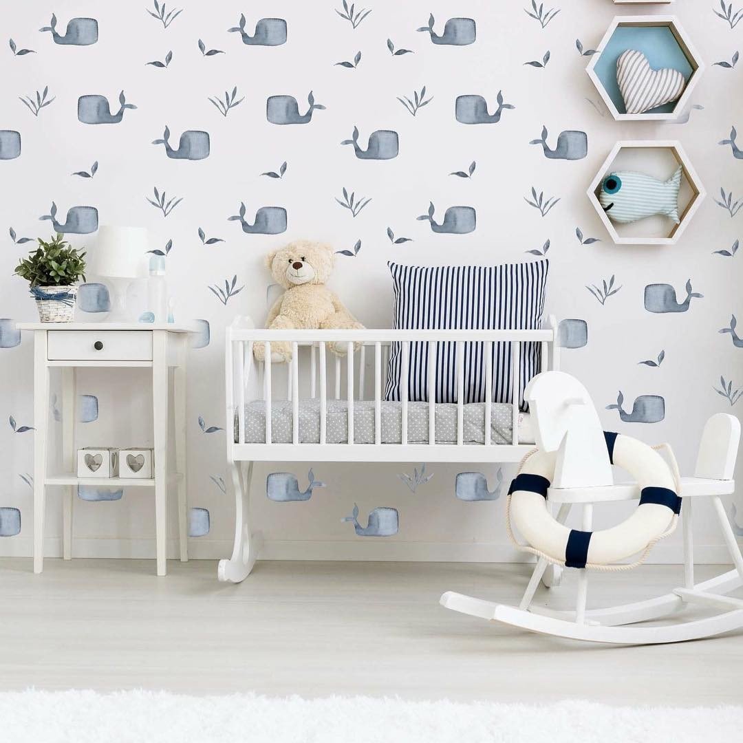 A bright, playful nursery with a white crib, a wall with small whale decals, and a rocking life preserver toy.
