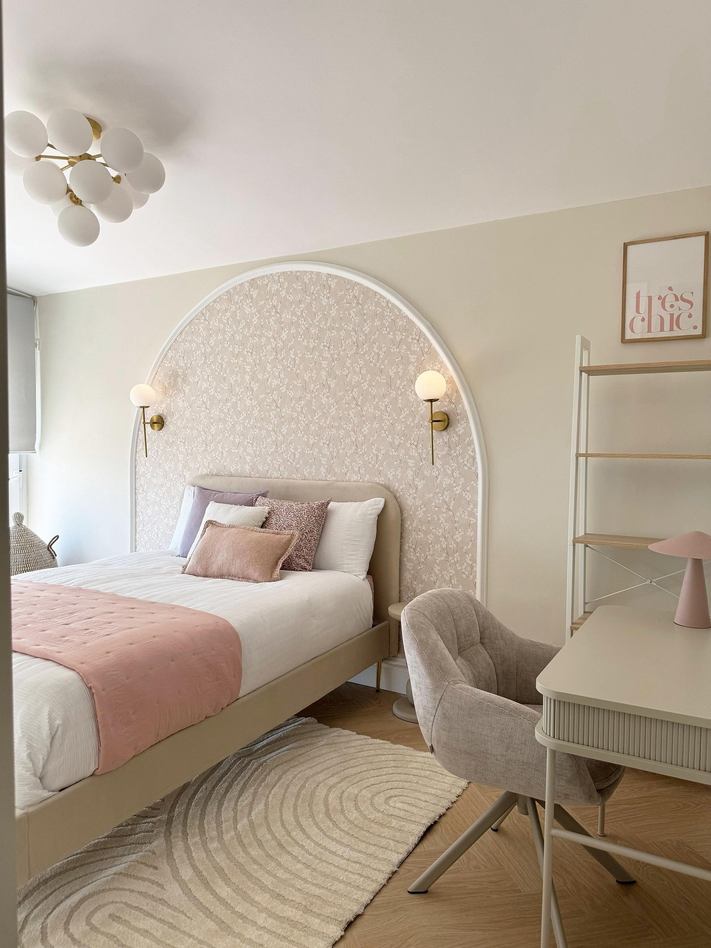  A chic girl's bedroom with a large arched, textured headboard, a pale pink duvet, and a stylish vanity desk.