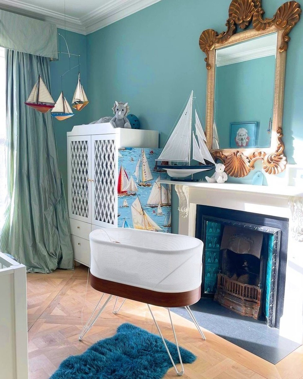 A classic nautical-themed nursery with a fireplace, a large gold-framed mirror, and sailboat decorations.