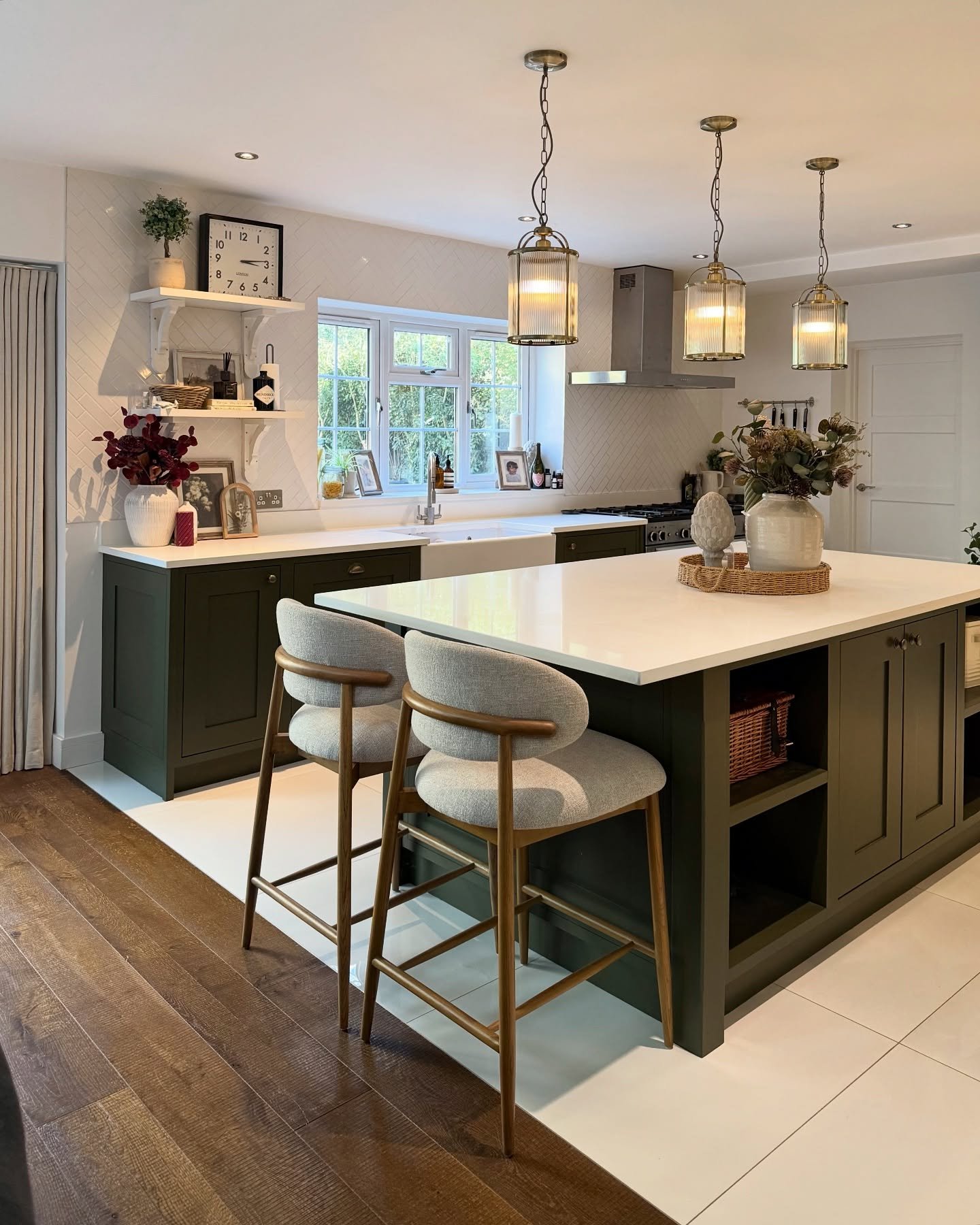 A dark green kitchen island with a white countertop and two upholstered bar stools in a cozy, elegant kitchen.