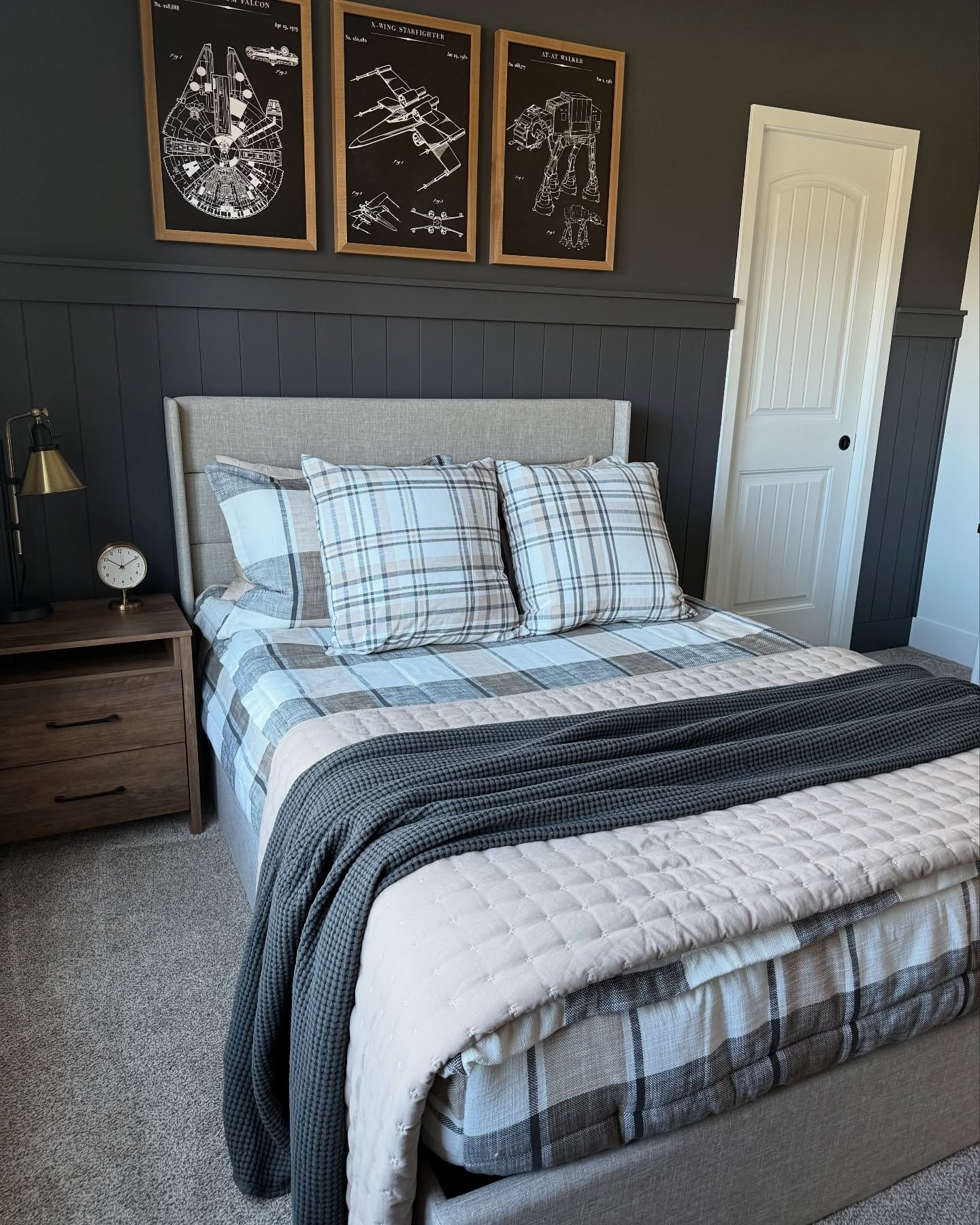 A dark gray bedroom with a bed featuring plaid bedding and a triptych of framed Star Wars blueprint art on the wall.