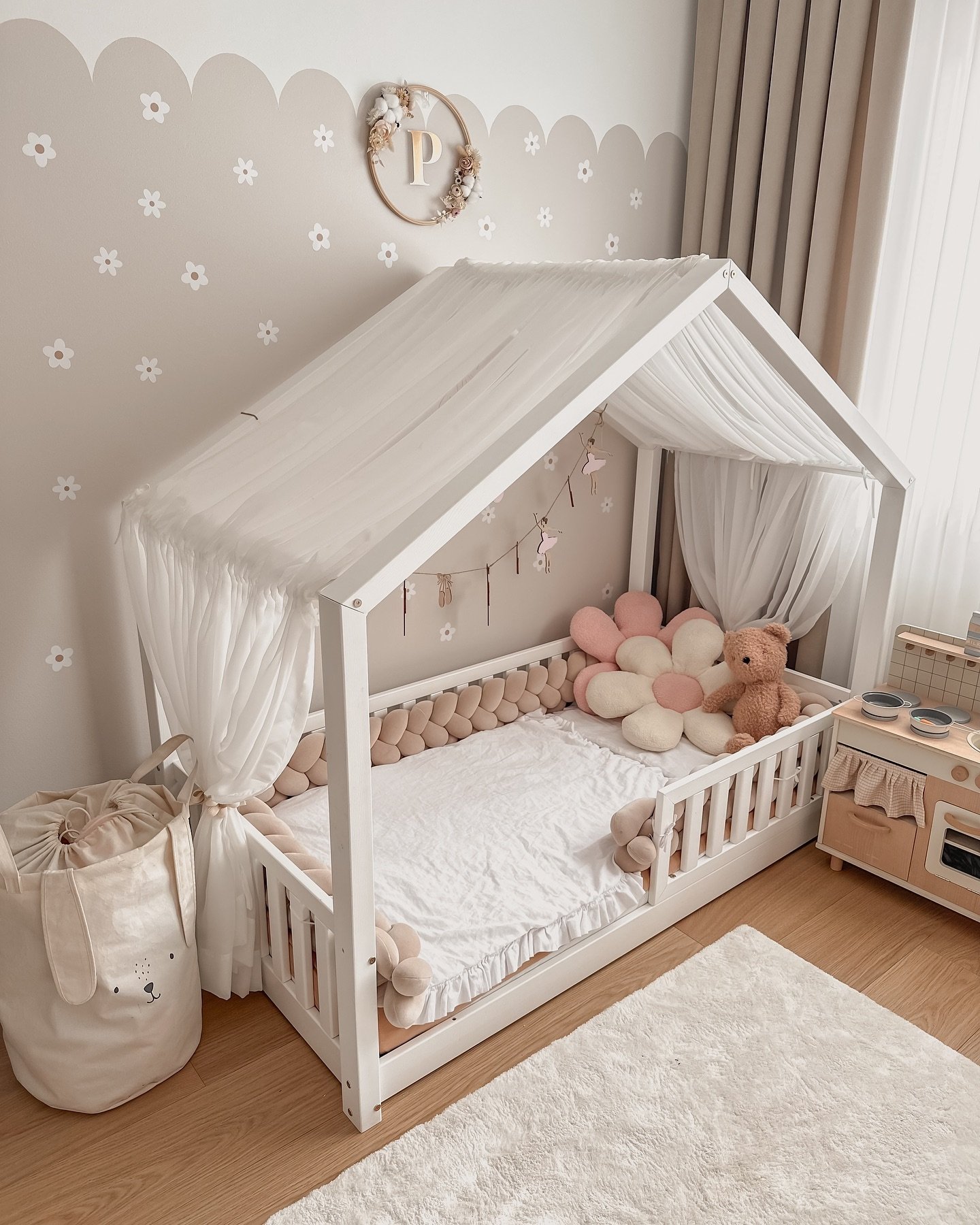 A cozy toddler room with a white house-frame bed, floral wall decals, and a toy kitchen.