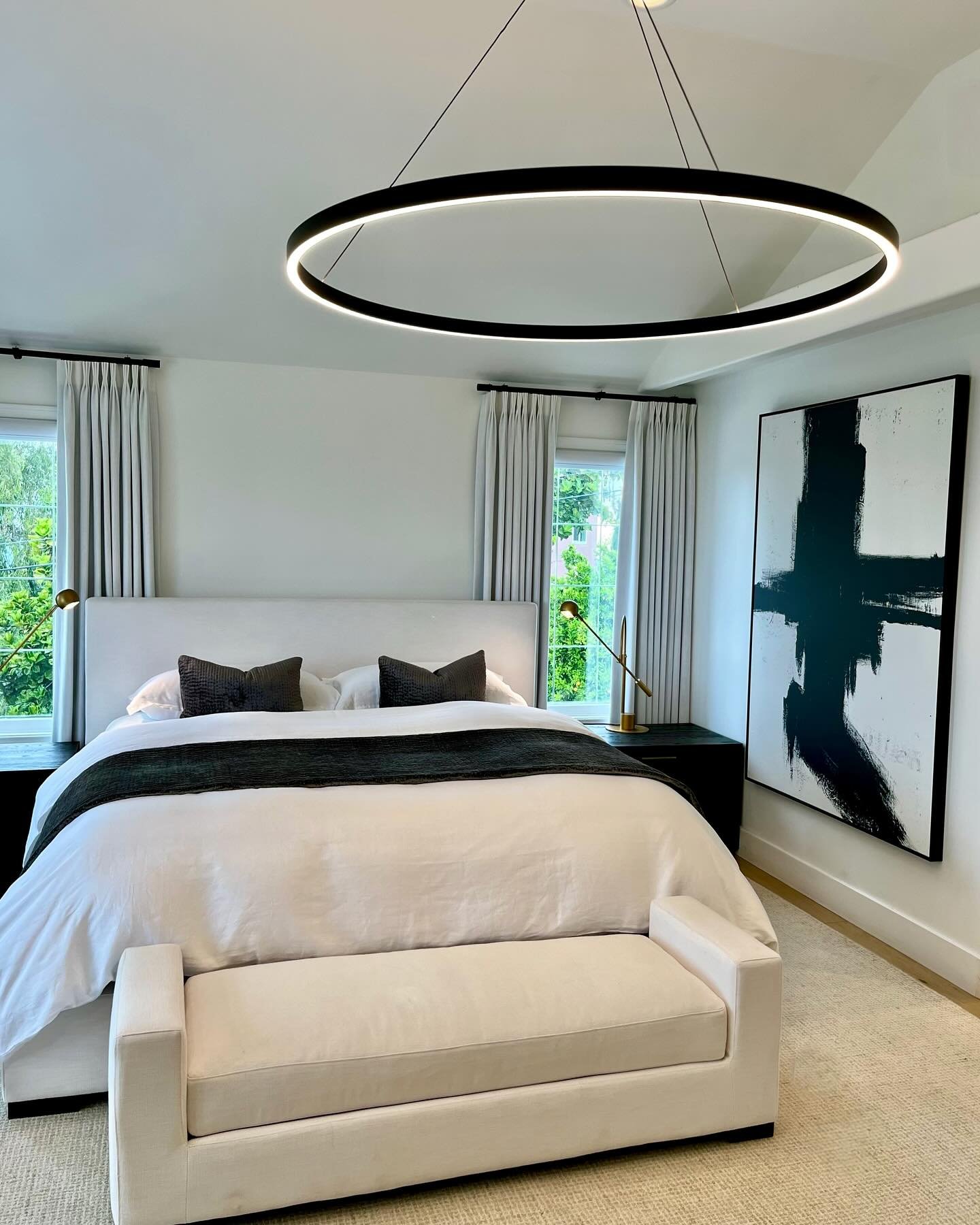 A luxurious and modern bedroom featuring a large abstract black and white painting, a plush white bed, a large circular LED chandelier, and sleek black nightstands.