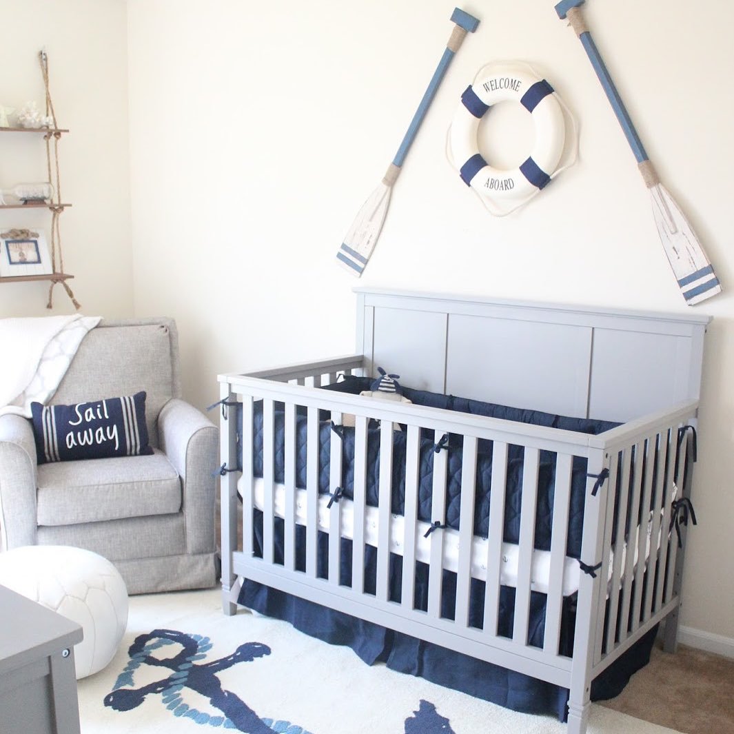 A classic nautical nursery with a gray crib, navy bedding, a life preserver, and decorative oars on the wall.