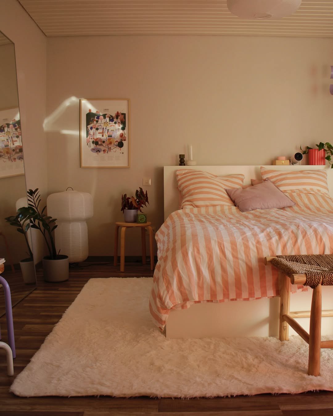 A soft, off-white shag rug is placed at the foot of a bed with pink and white striped bedding in a cozy bedroom.