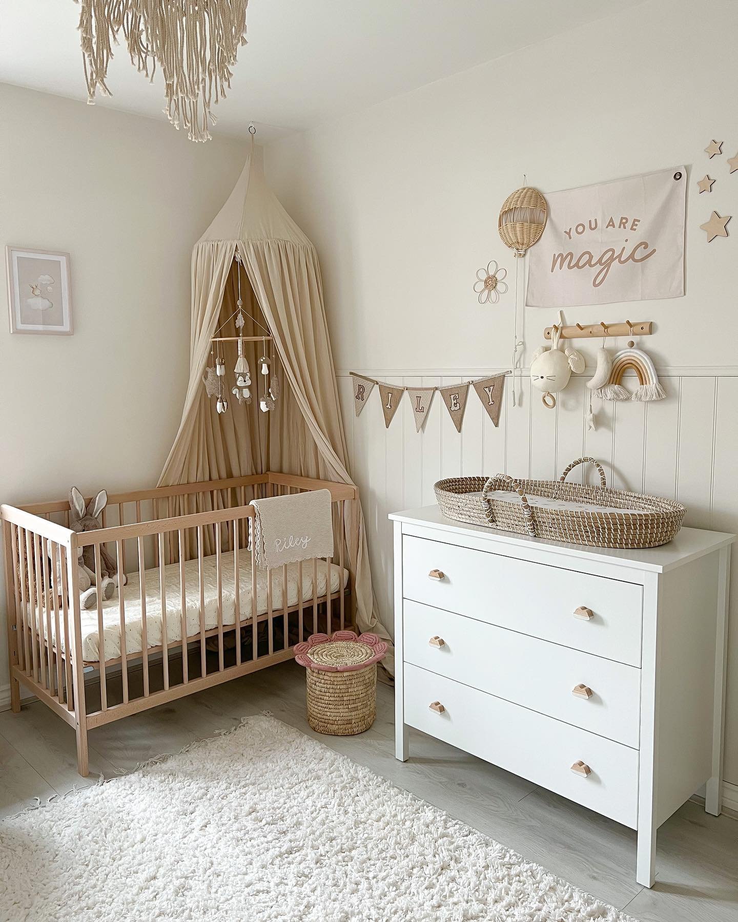 A boho-chic nursery with a light wood crib, white dresser, and macramé light fixture.