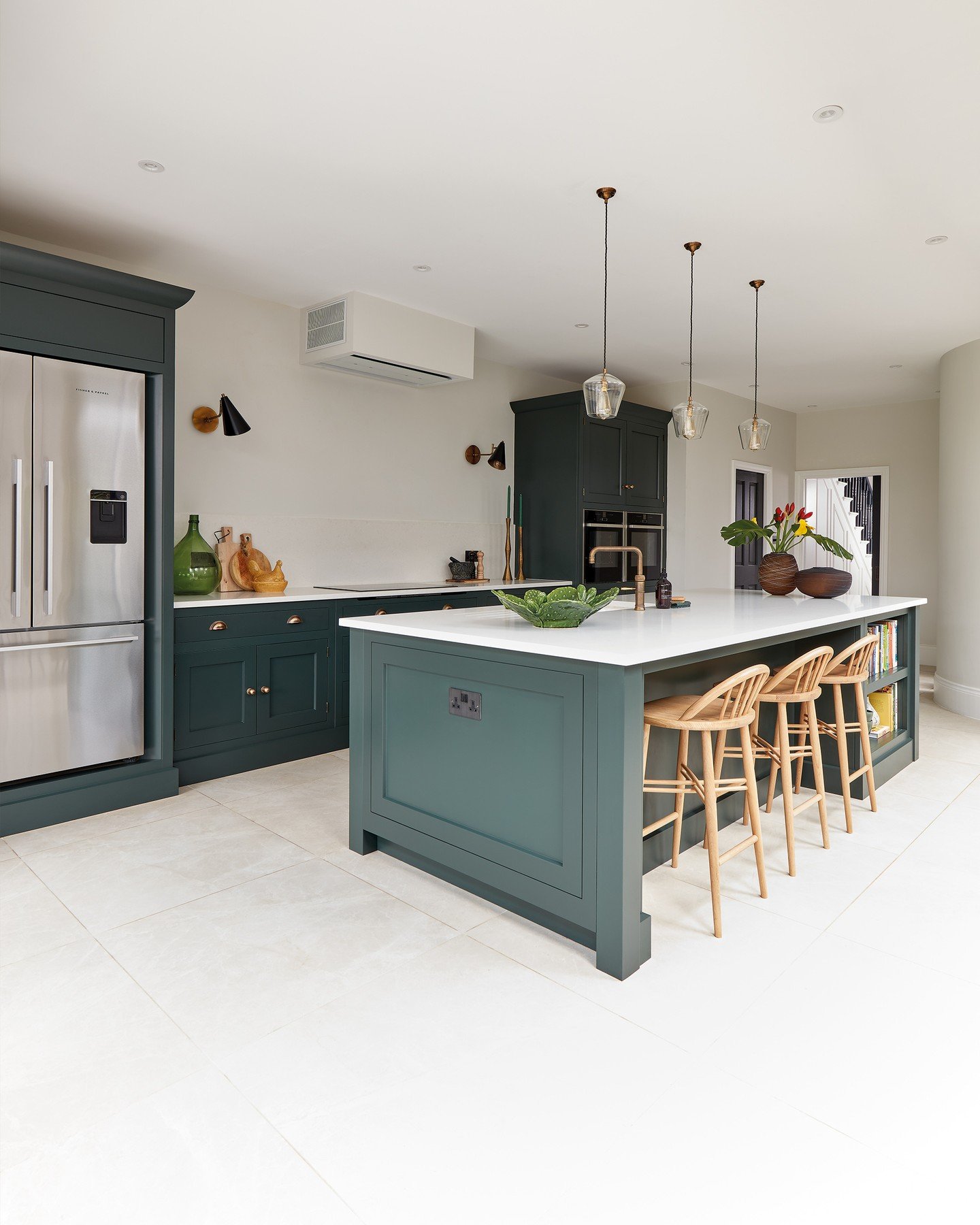 A large, sage green kitchen island with a white countertop and four light wood bar stools in a bright kitchen.