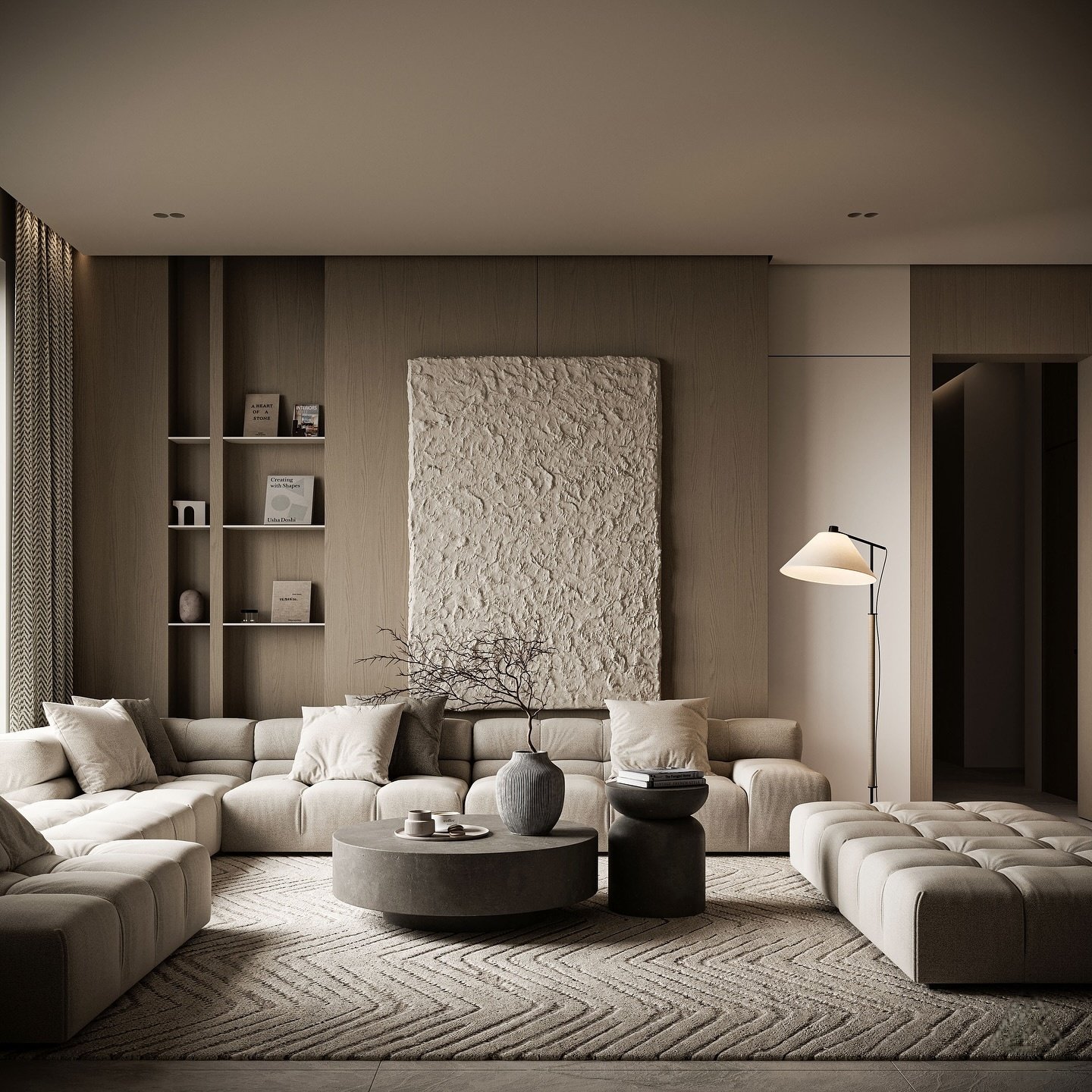 A contemporary living room with a large, low-profile modular sofa, a round gray coffee table, and a textured, abstract art piece on the wall.