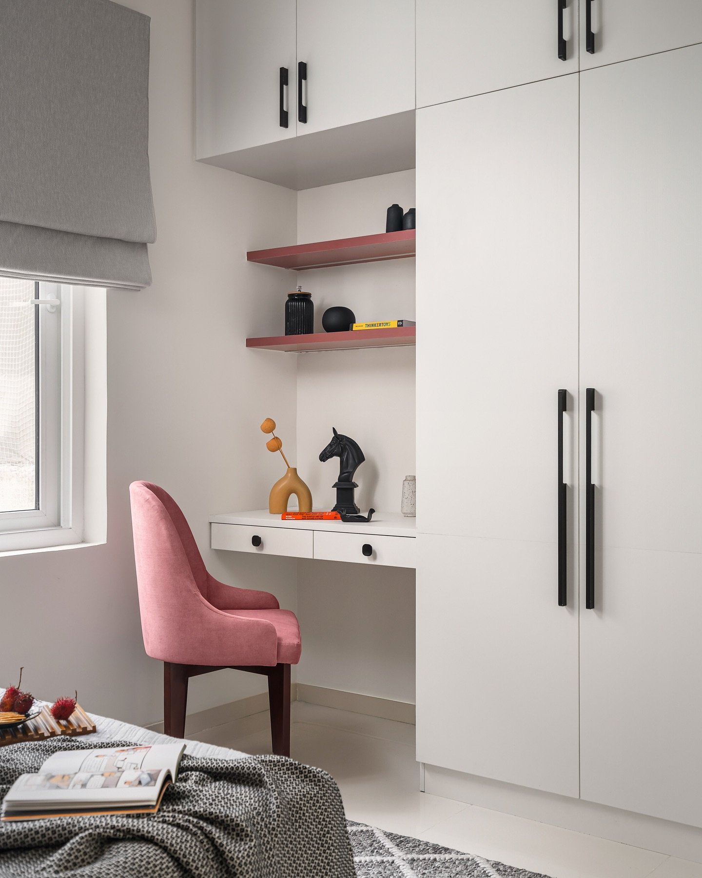A compact study desk integrated into a white cabinet system, with a pink upholstered chair and two floating shelves above.