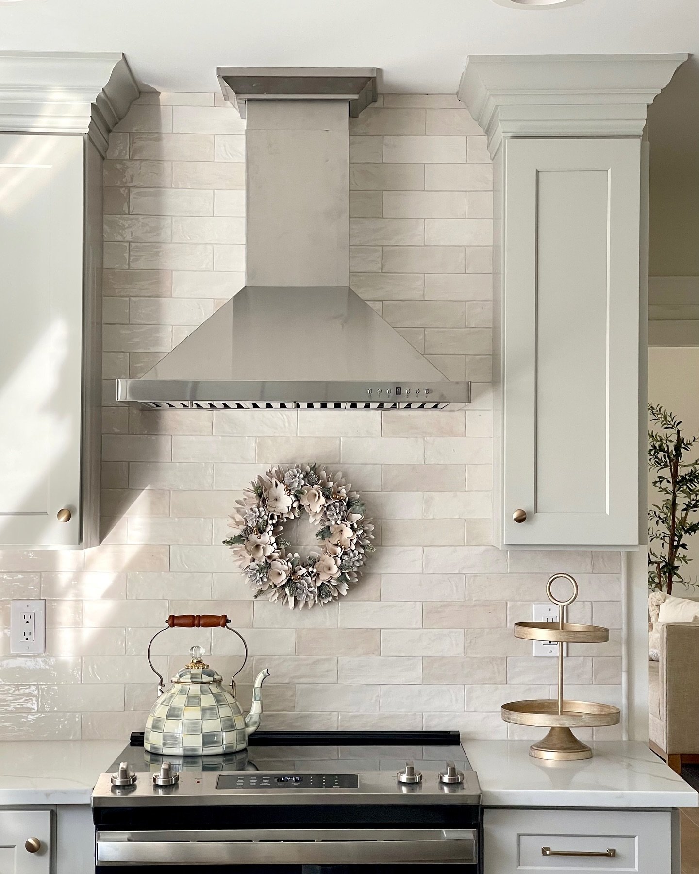 A kitchen featuring a glossy, handmade-look subway tile backsplash with subtle color variations, installed behind a stovetop with a stainless steel range hood.