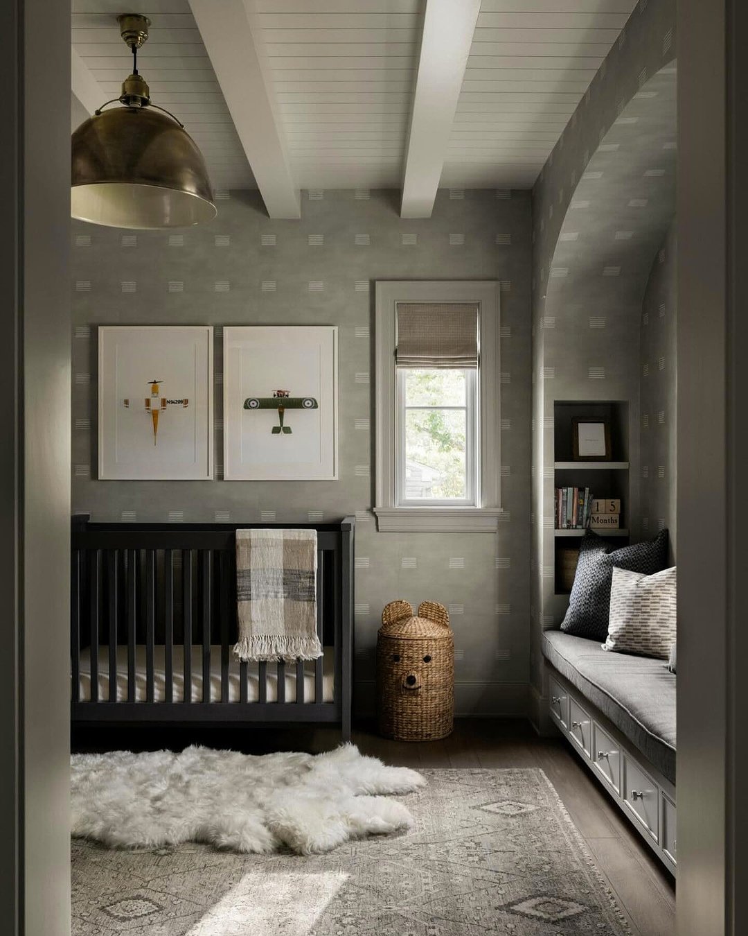 A modern nursery with a dark wood crib, airplane art, and a built-in reading nook.