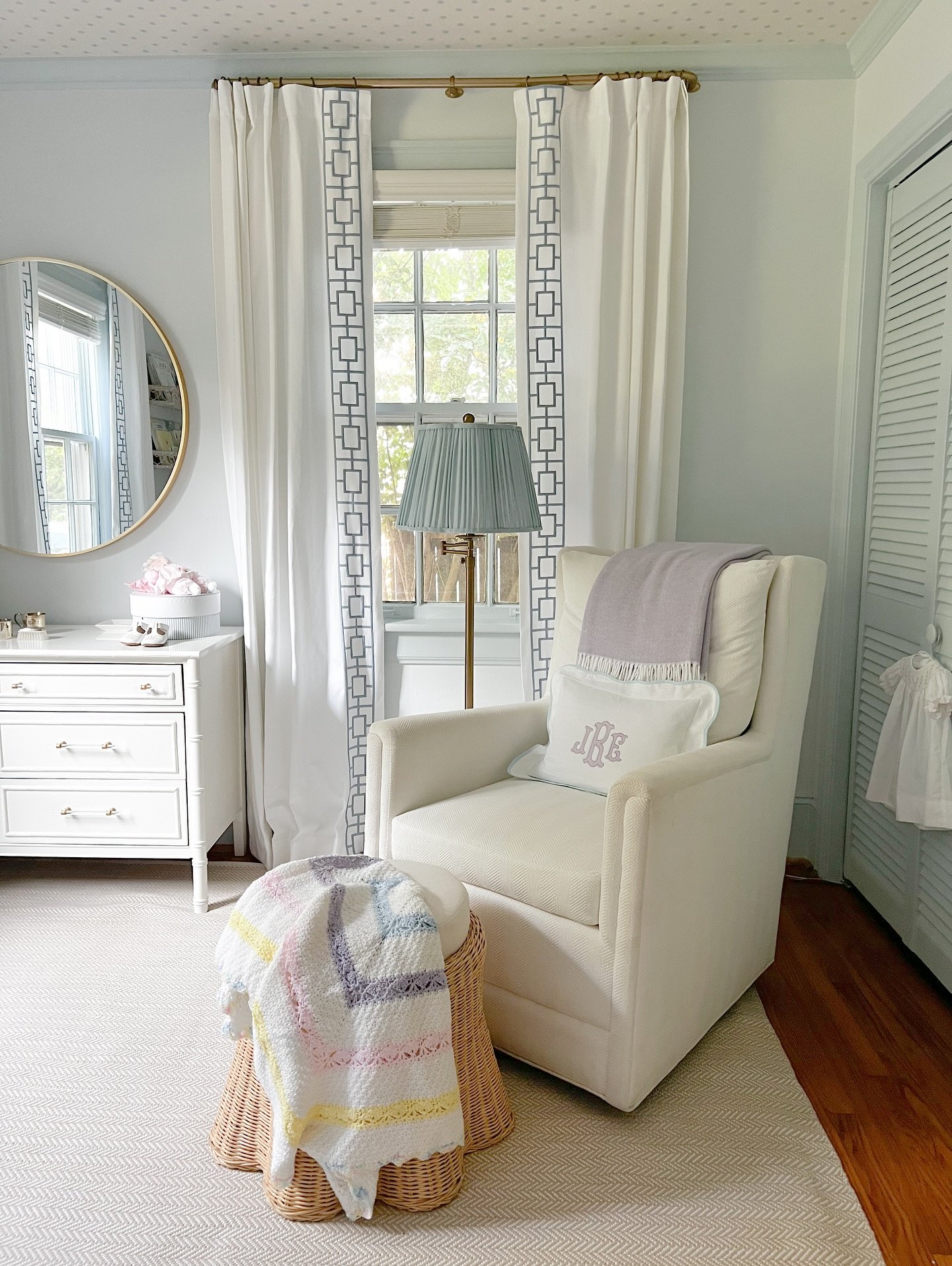 A chic nursery corner with an off-white glider chair, a wicker stool, and elegant curtains.