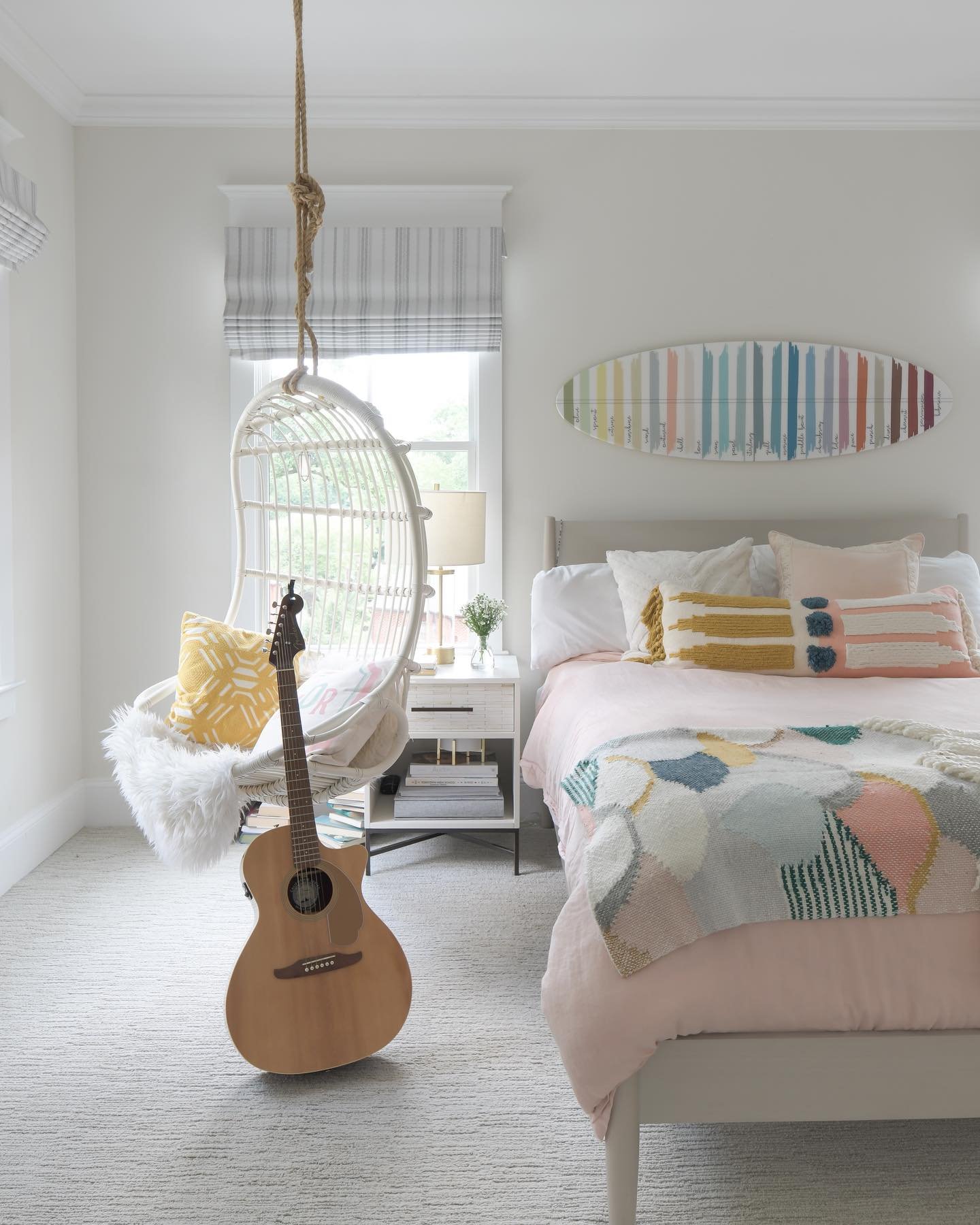A bright and airy teen bedroom with a bohemian style, featuring a hanging egg chair, a guitar, and a decorative surfboard.