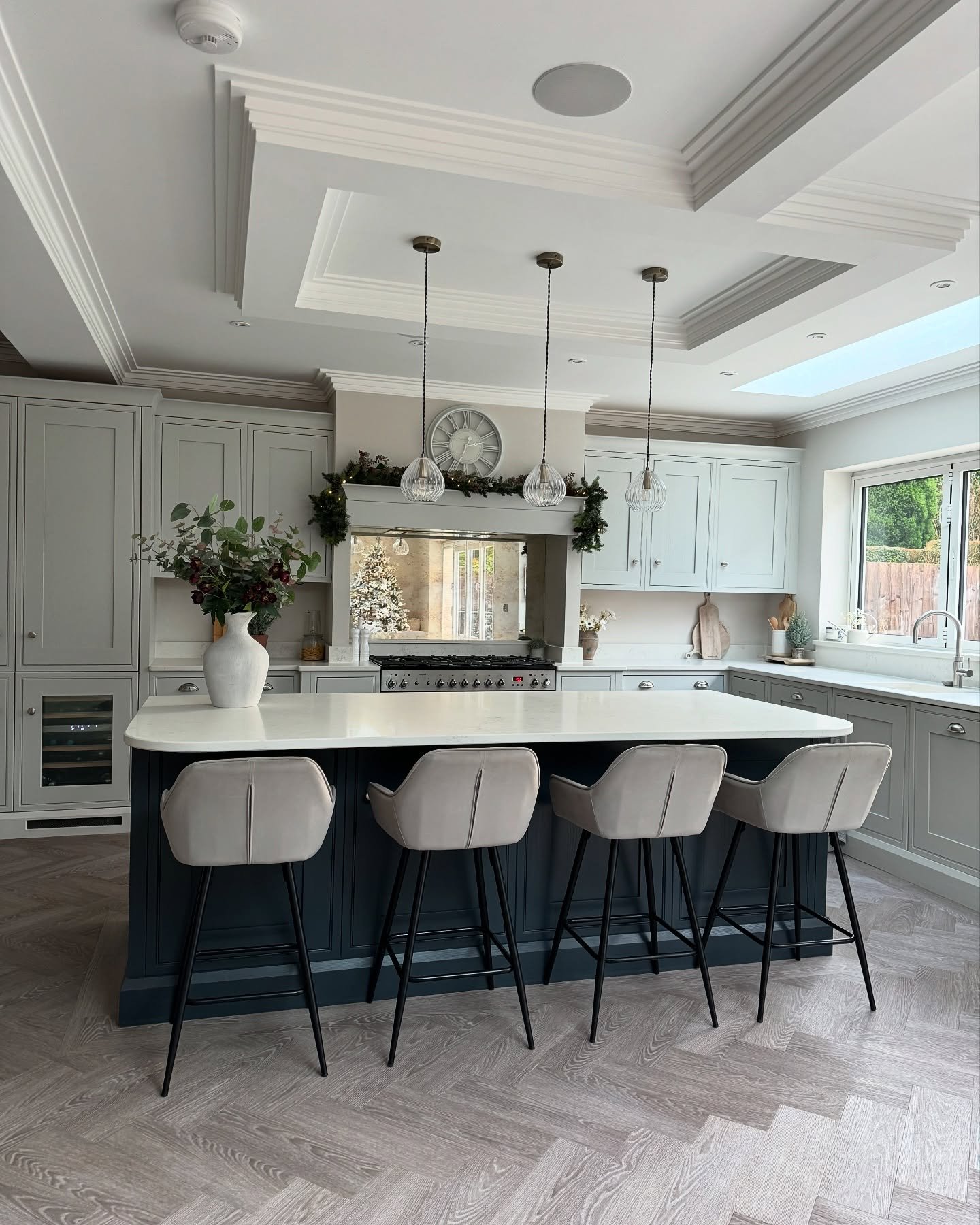 A dark blue kitchen island with a white countertop and four light gray upholstered bar stools in an elegant, well-lit kitchen.