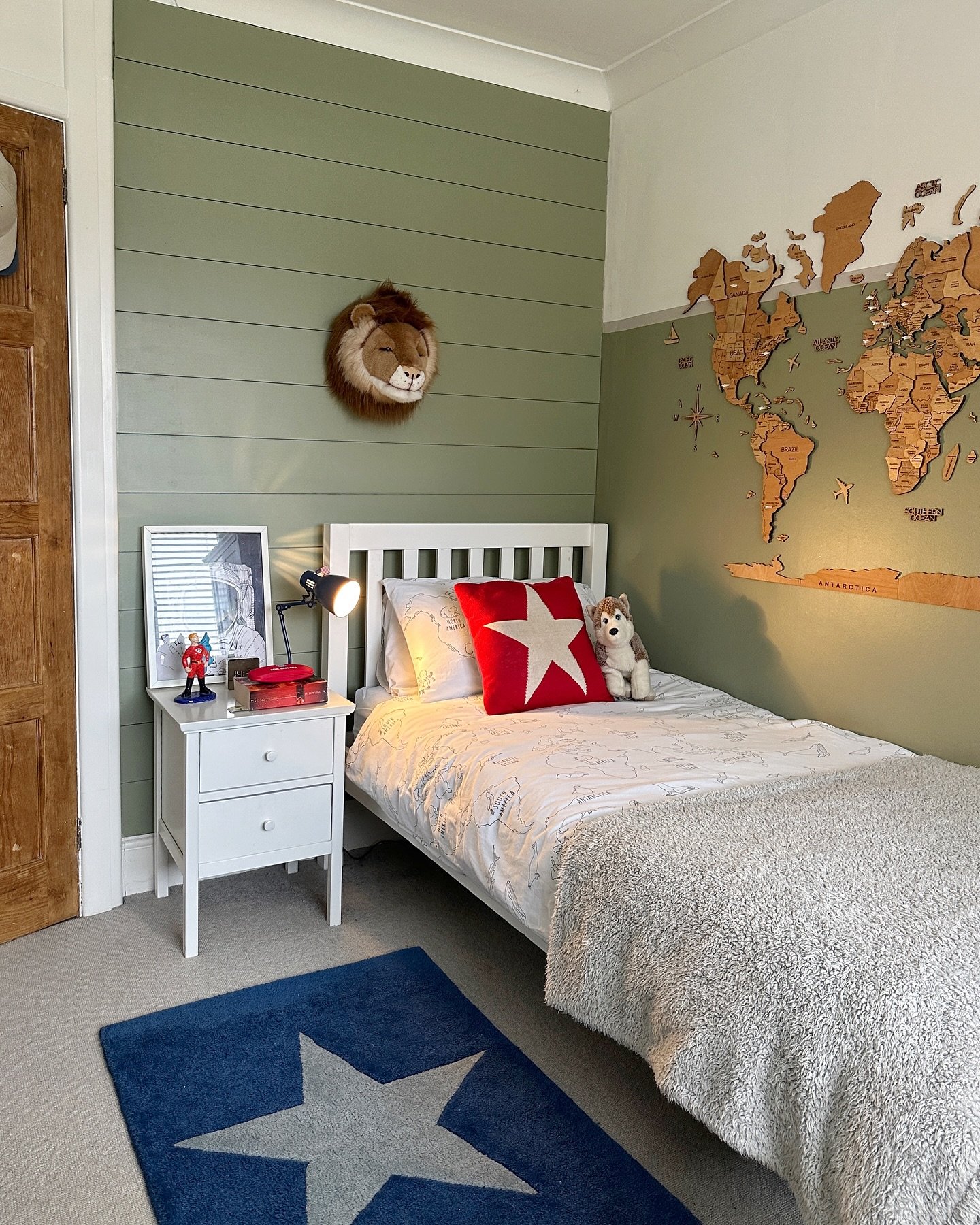A bedroom with a split-level green and white wall, a world map on the wall, and a twin bed with a red star pillow.