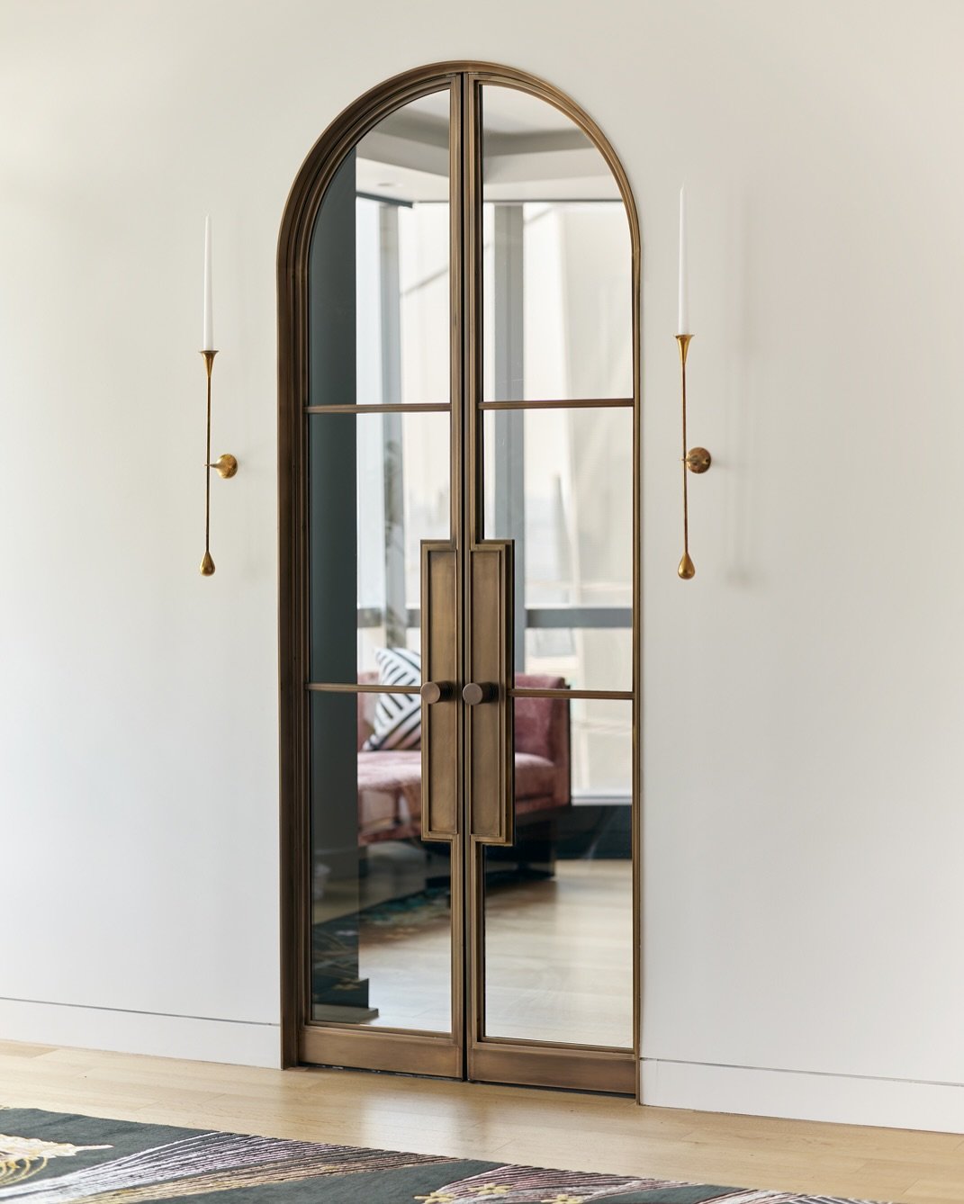A pair of elegant, arched double doors made of bronze-toned metal and clear glass, with a view into the room beyond.
