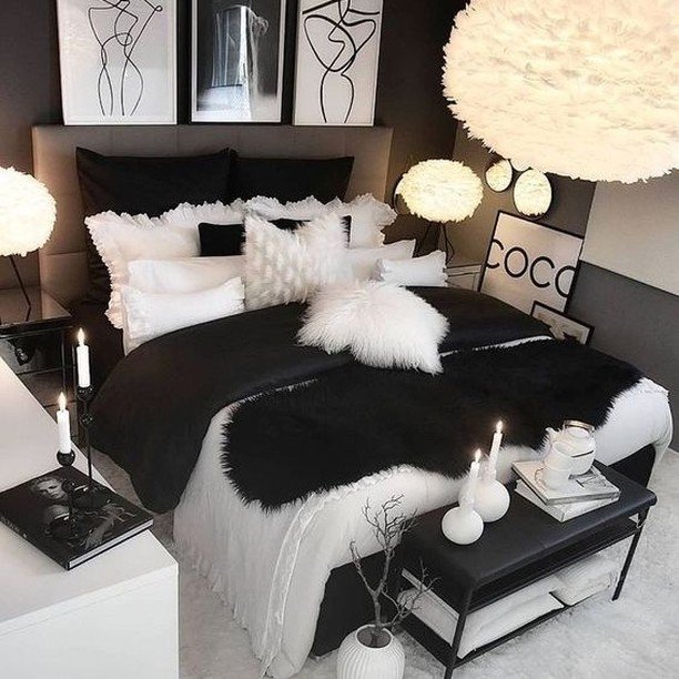 A cozy and luxurious black and white bedroom with a layered bed, a gallery wall of line art prints, and a large fluffy feather pendant light.