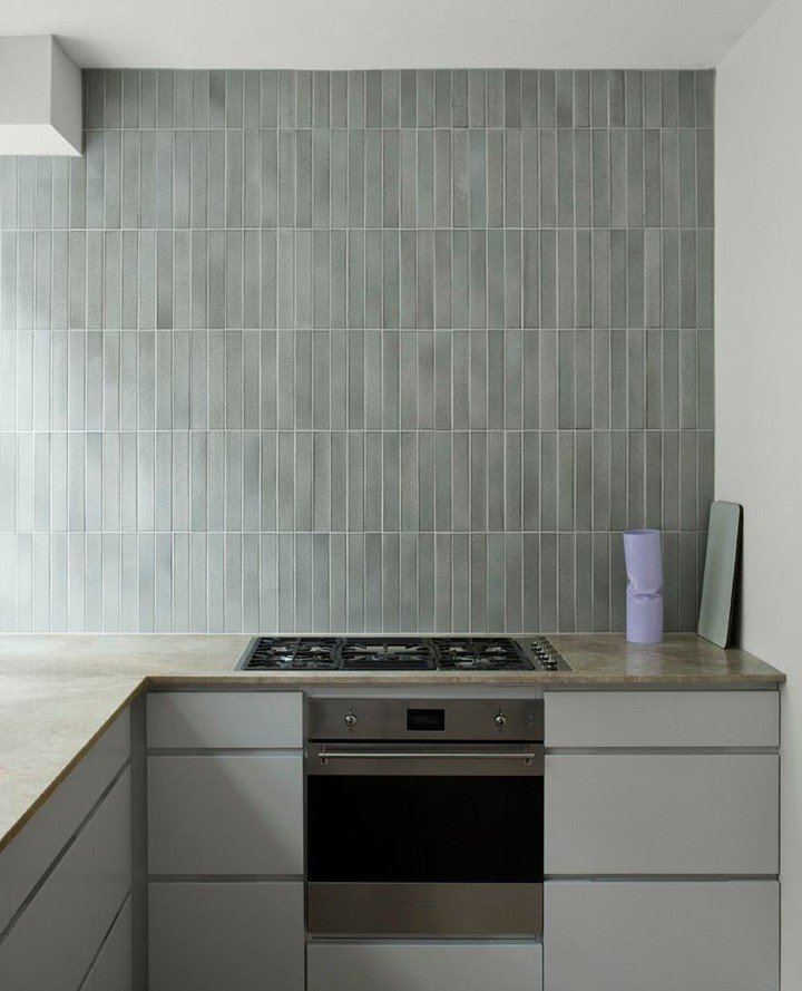 A contemporary kitchen with a floor-to-ceiling backsplash of narrow, gray vertical tiles, positioned behind a stovetop and oven unit.