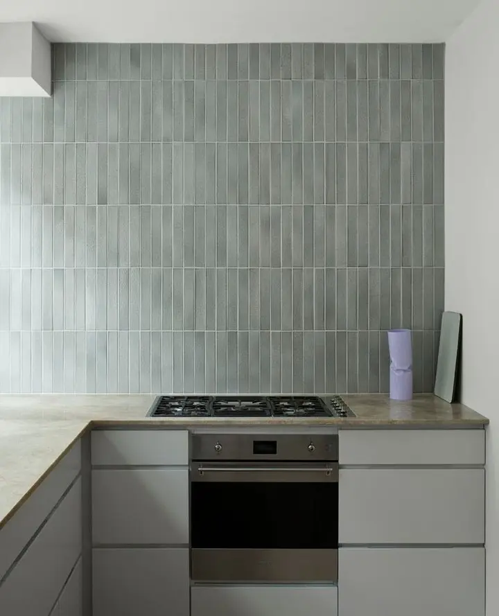 A contemporary kitchen with a floor-to-ceiling backsplash of narrow, gray vertical tiles, positioned behind a stovetop and oven unit.