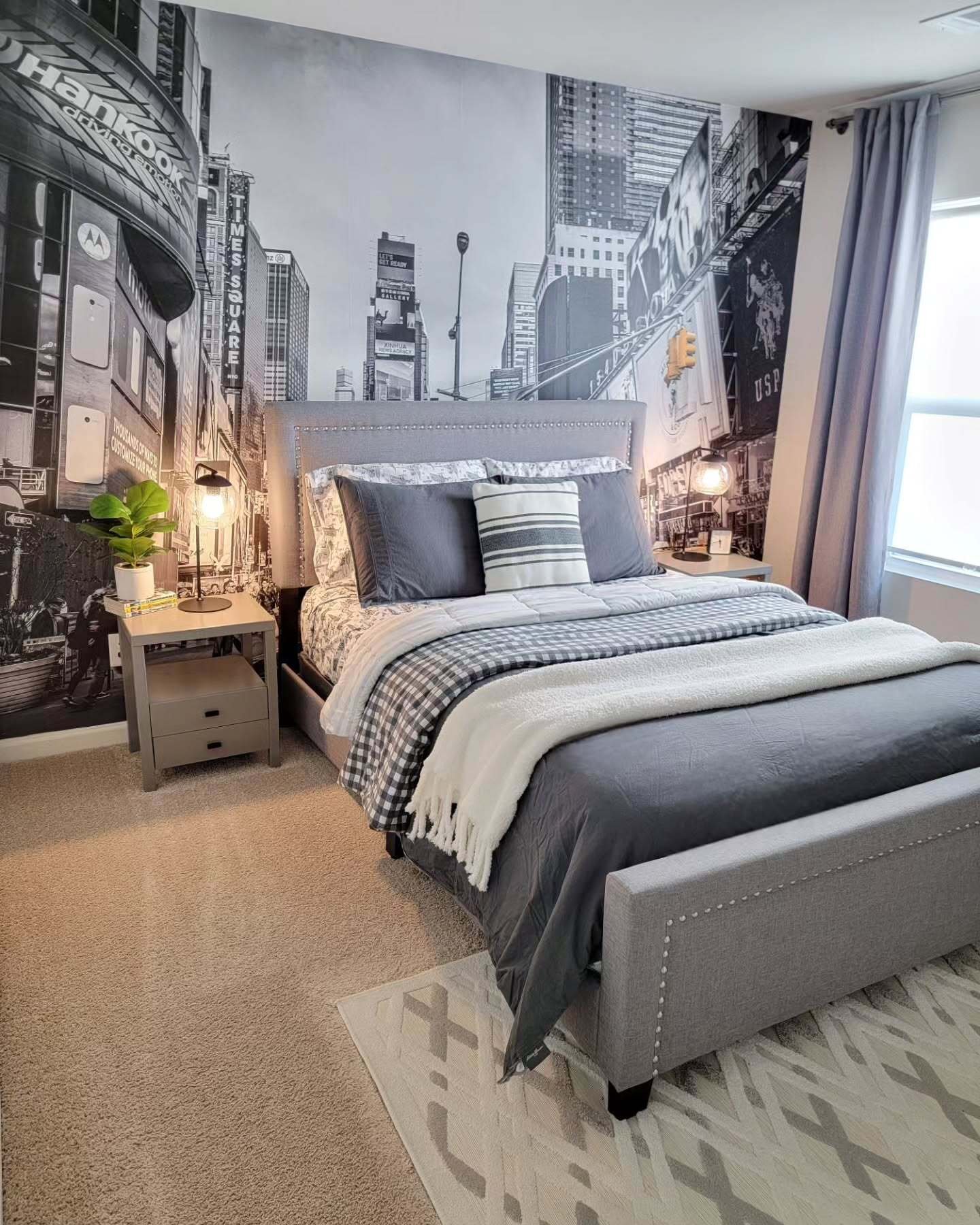 A teen's bedroom with a black and white Times Square mural wall, a gray upholstered bed, and modern industrial-style lighting.