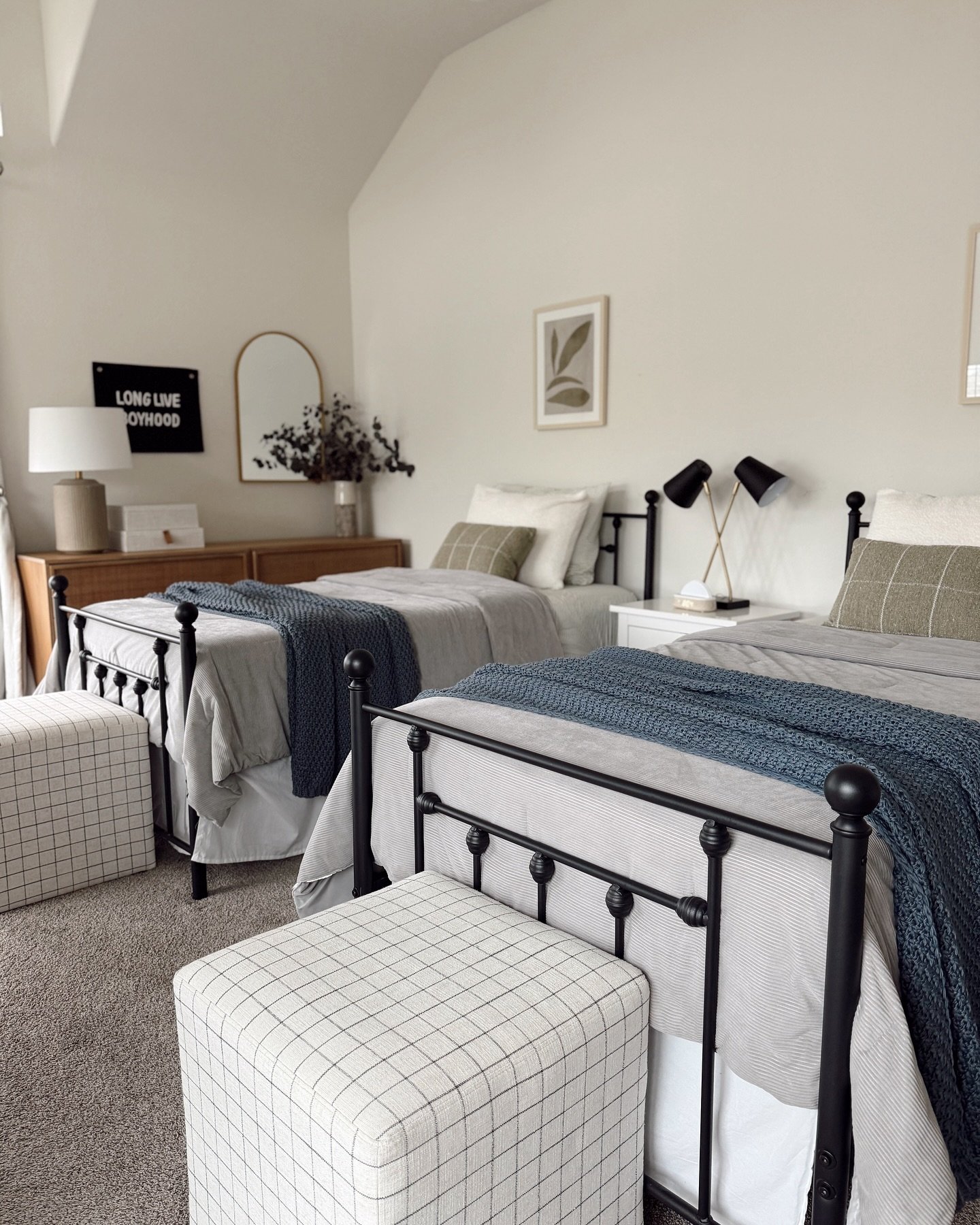 A shared bedroom with two twin metal-frame beds, a mid-century modern dresser, and a calm, neutral color scheme.