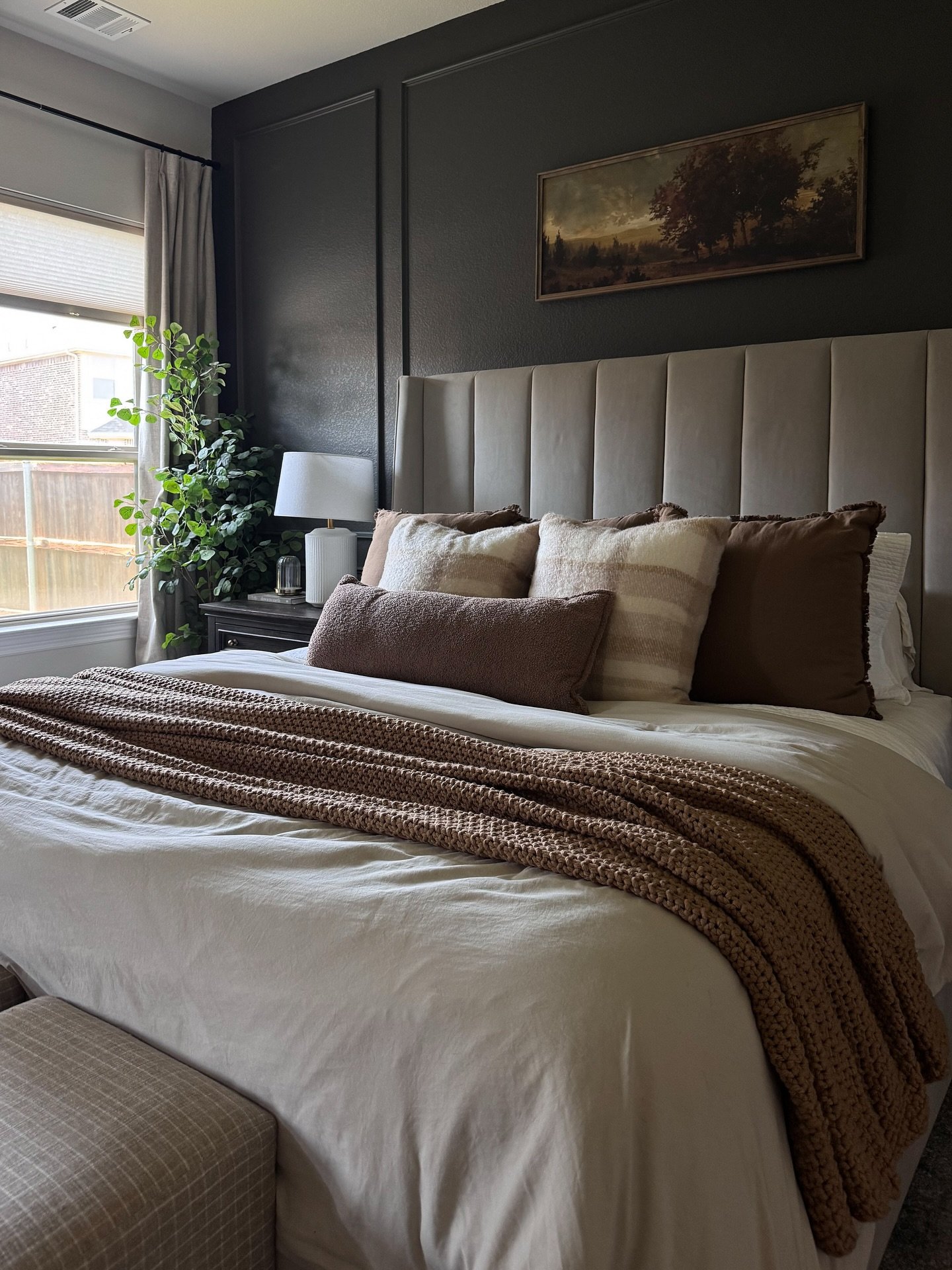A bedroom with a dark gray paneled accent wall, a gray upholstered headboard, and a bed layered with cozy brown and cream blankets.