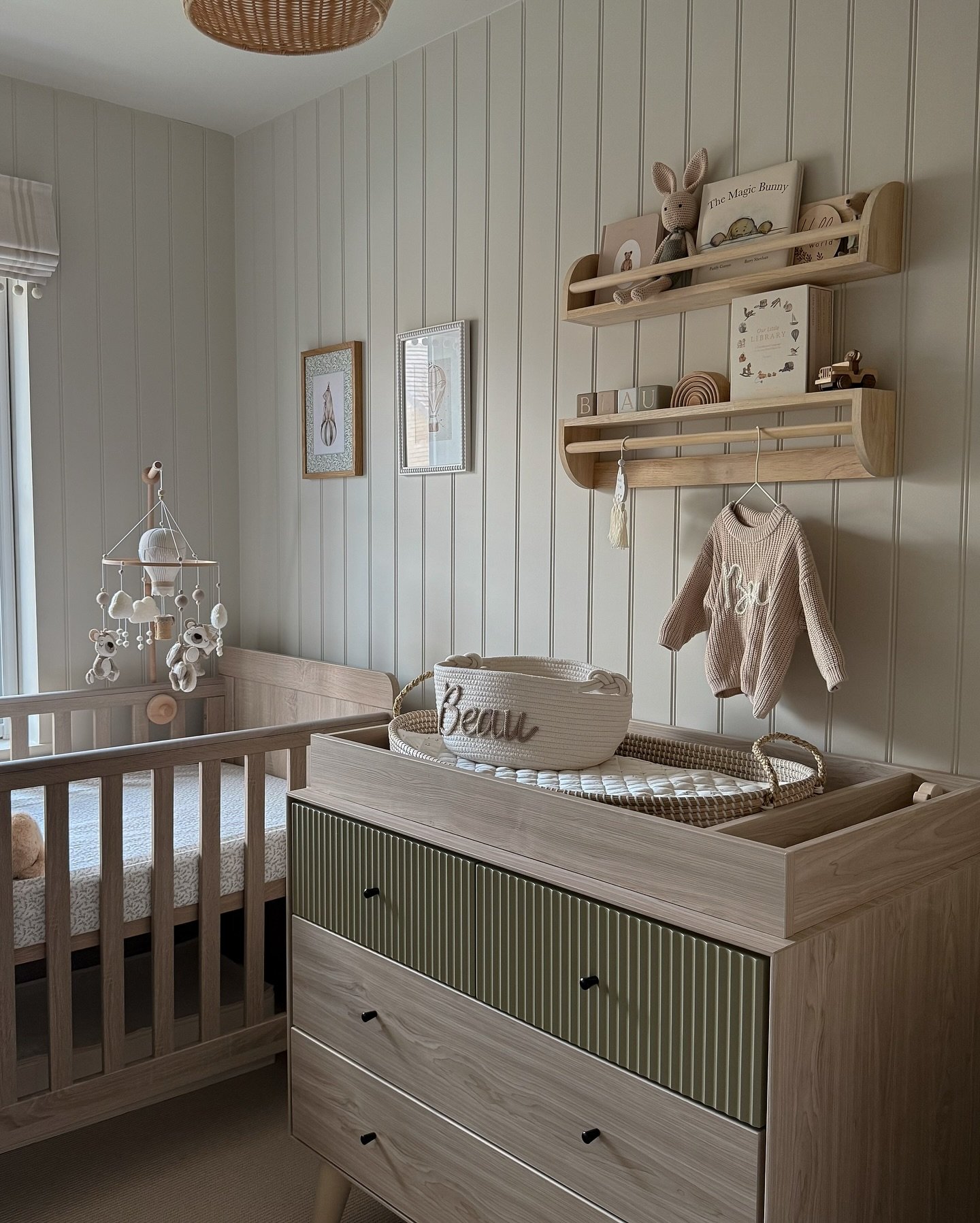 A Scandinavian-style nursery with light wood furniture, a paneled beige wall, and natural textures.