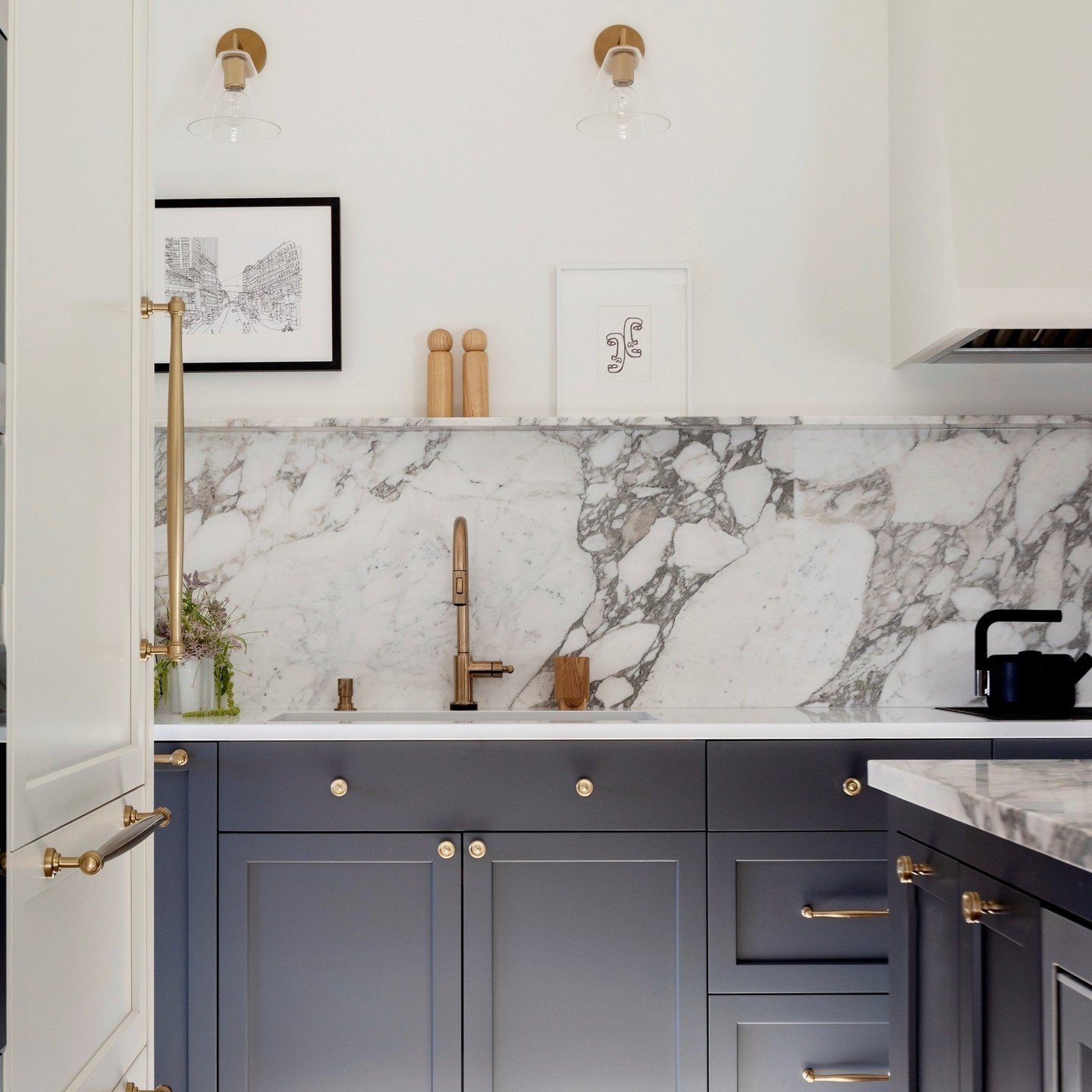 A kitchen featuring a luxurious, single-slab marble backsplash with prominent gray veining, set above dark gray cabinets with gold hardware.