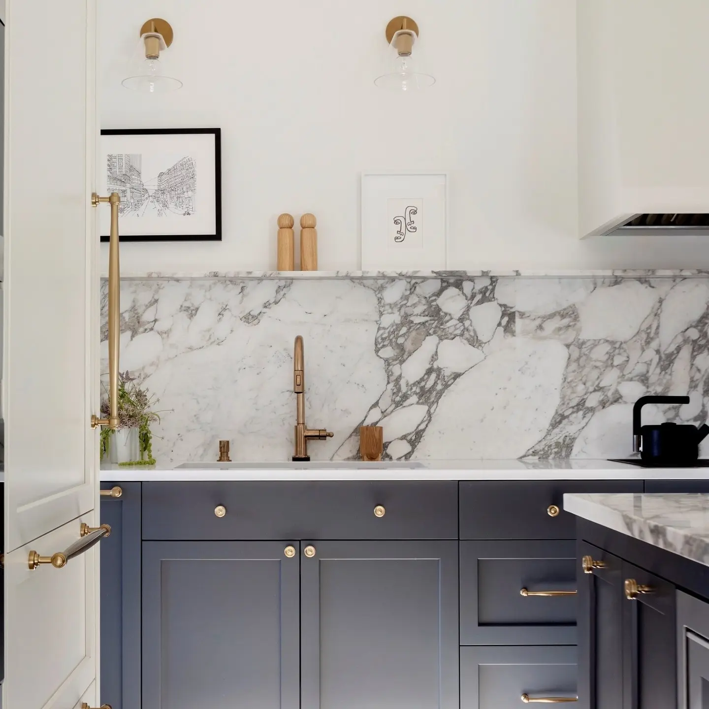 A kitchen featuring a luxurious, single-slab marble backsplash with prominent gray veining, set above dark gray cabinets with gold hardware.
