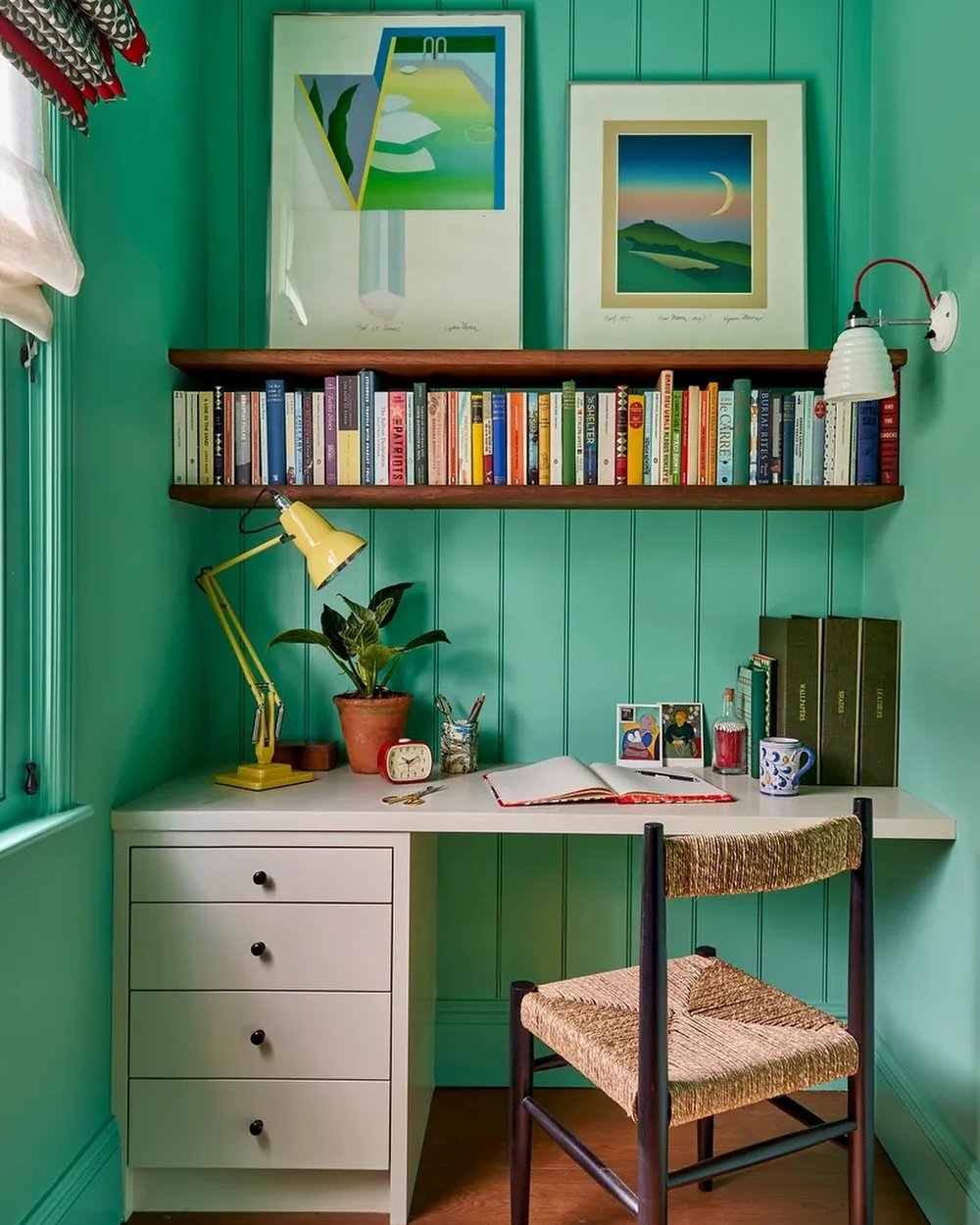 A vibrant study corner featuring a built-in white desk with four drawers, a long wooden bookshelf above, and a woven chair.