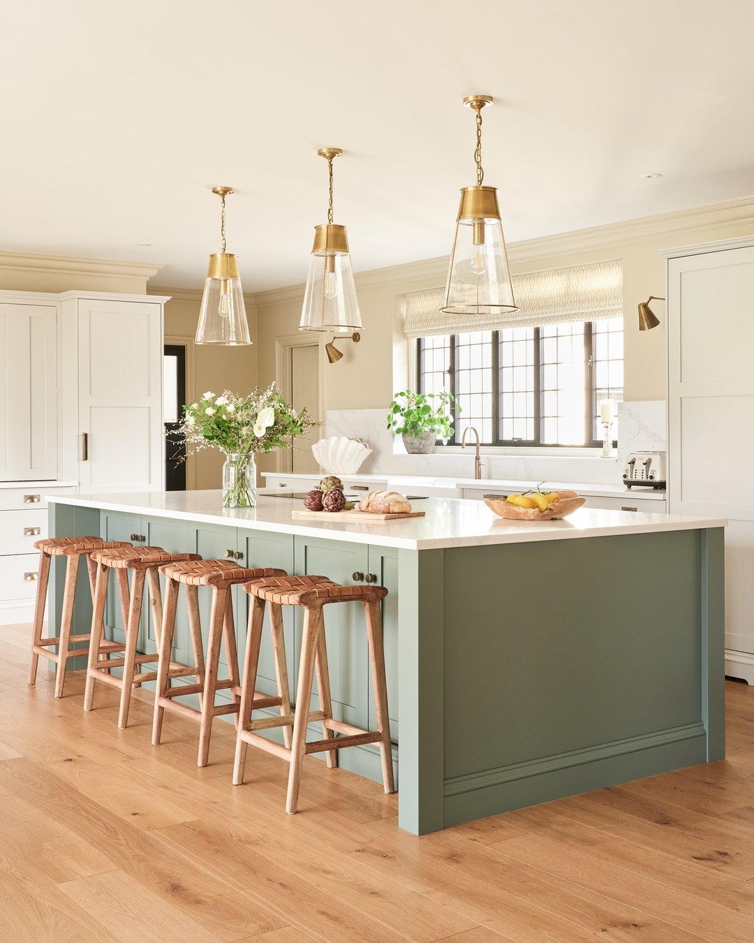A large sage green kitchen island with a white countertop and five wooden bar stools in a bright, traditional-style kitchen.