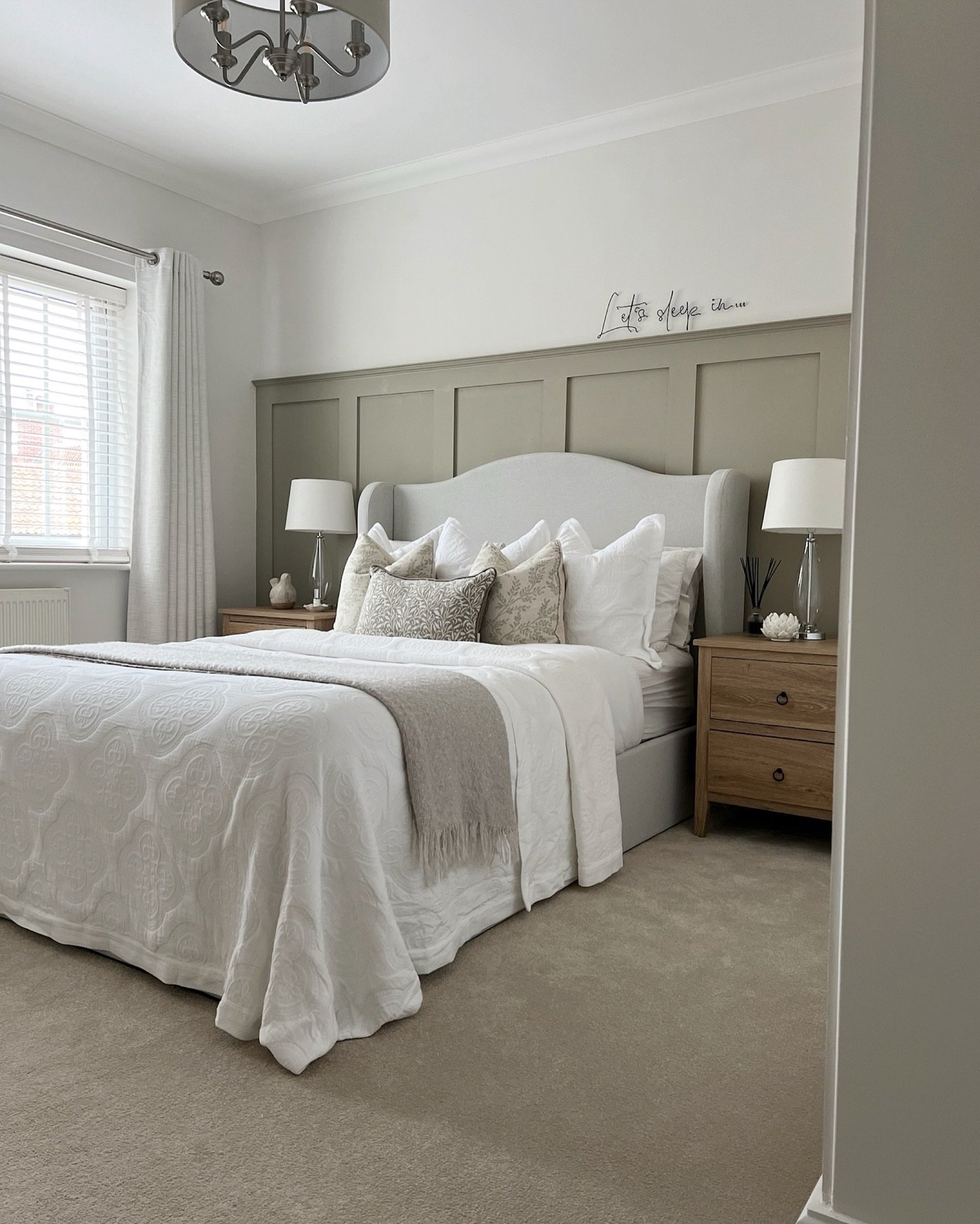 A tranquil guest bedroom with a gray upholstered bed and headboard, layered white and gray bedding, and a board and batten accent wall. The room is decorated with matching wood nightstands and modern table lamps.