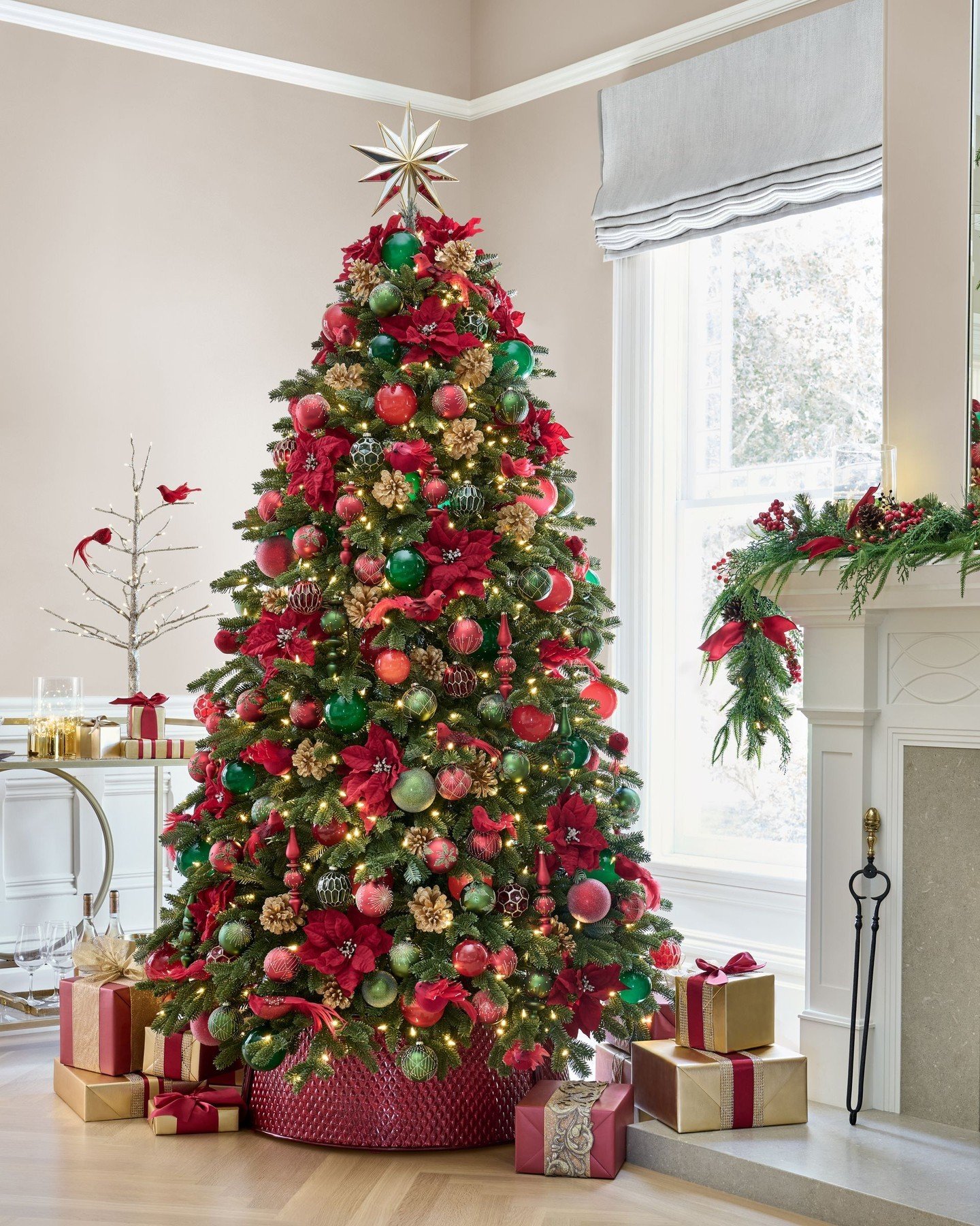 A fully decorated Christmas tree in a traditional red and green color scheme, featuring poinsettias and a gold star topper.