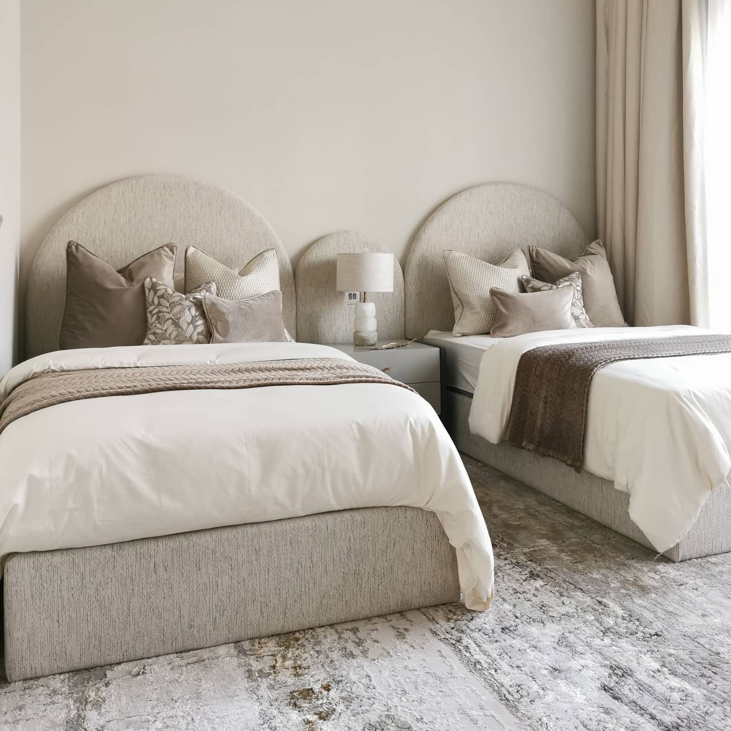 A pair of twin beds with arched beige headboards and neutral-colored bedding in a cozy bedroom.