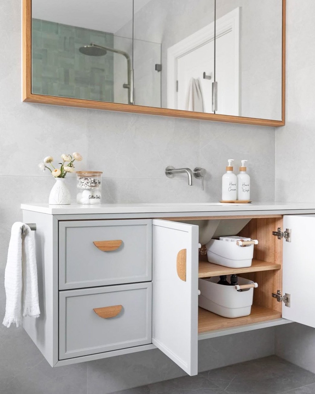 Floating light grey bathroom vanity with open cabinet door revealing wooden shelves, white storage bins, and two light grey drawers.