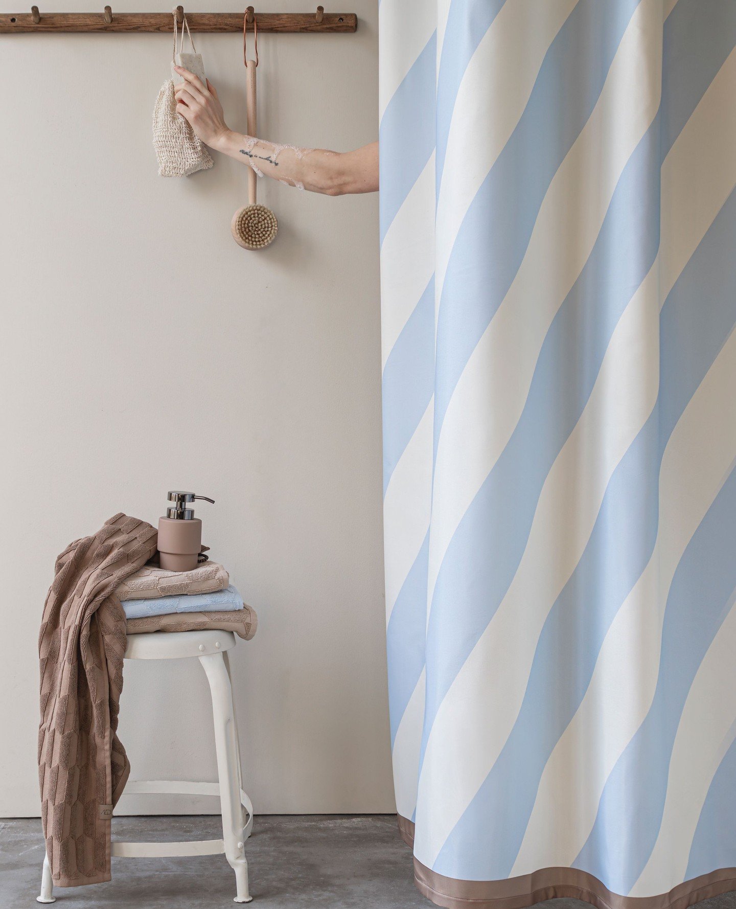 A blue and white diagonal wavy striped shower curtain next to a white stool holding towels and a soap dispenser.