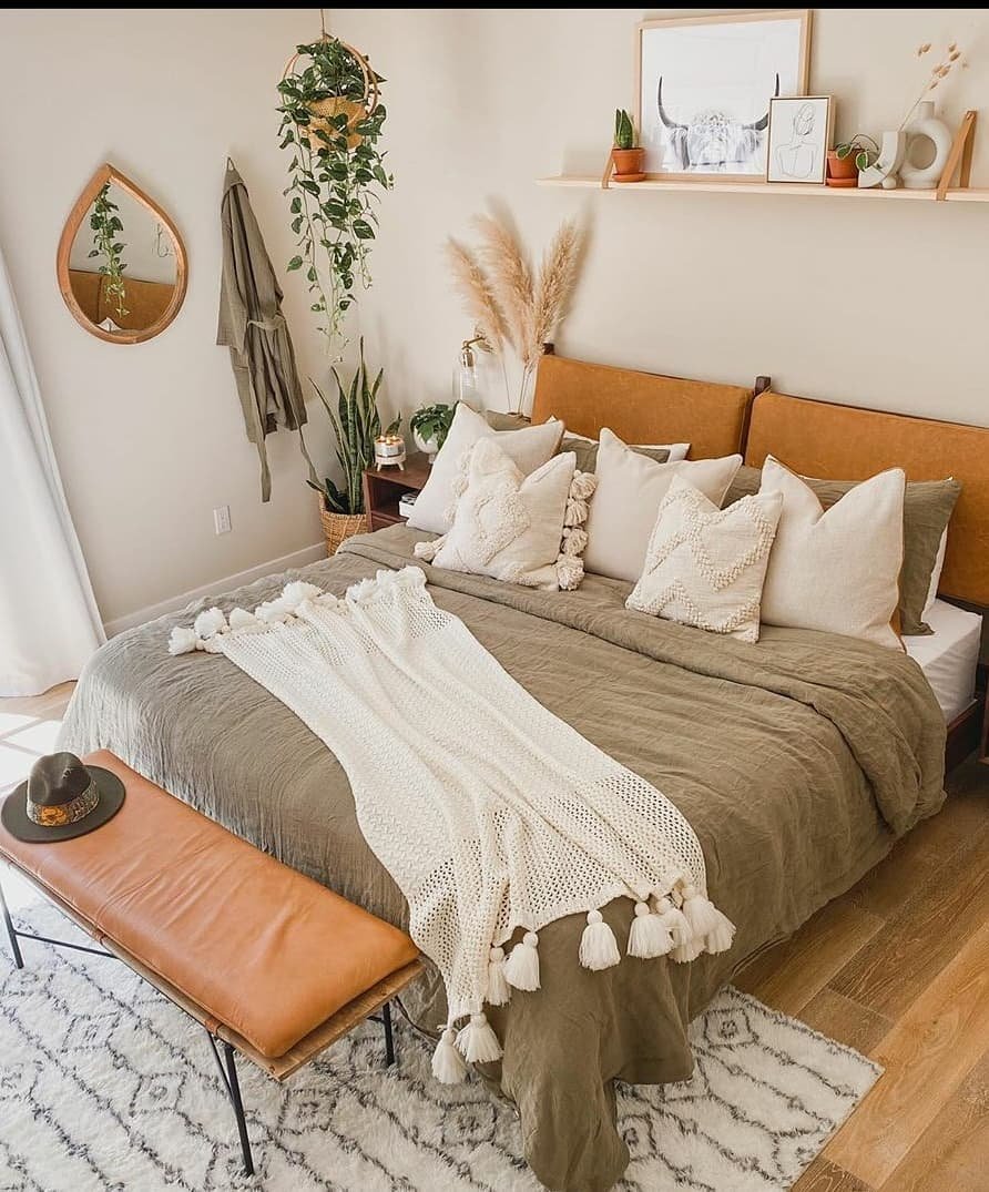 A modern boho bedroom with a leather headboard and bench, a green comforter, and a clean, minimalist aesthetic.