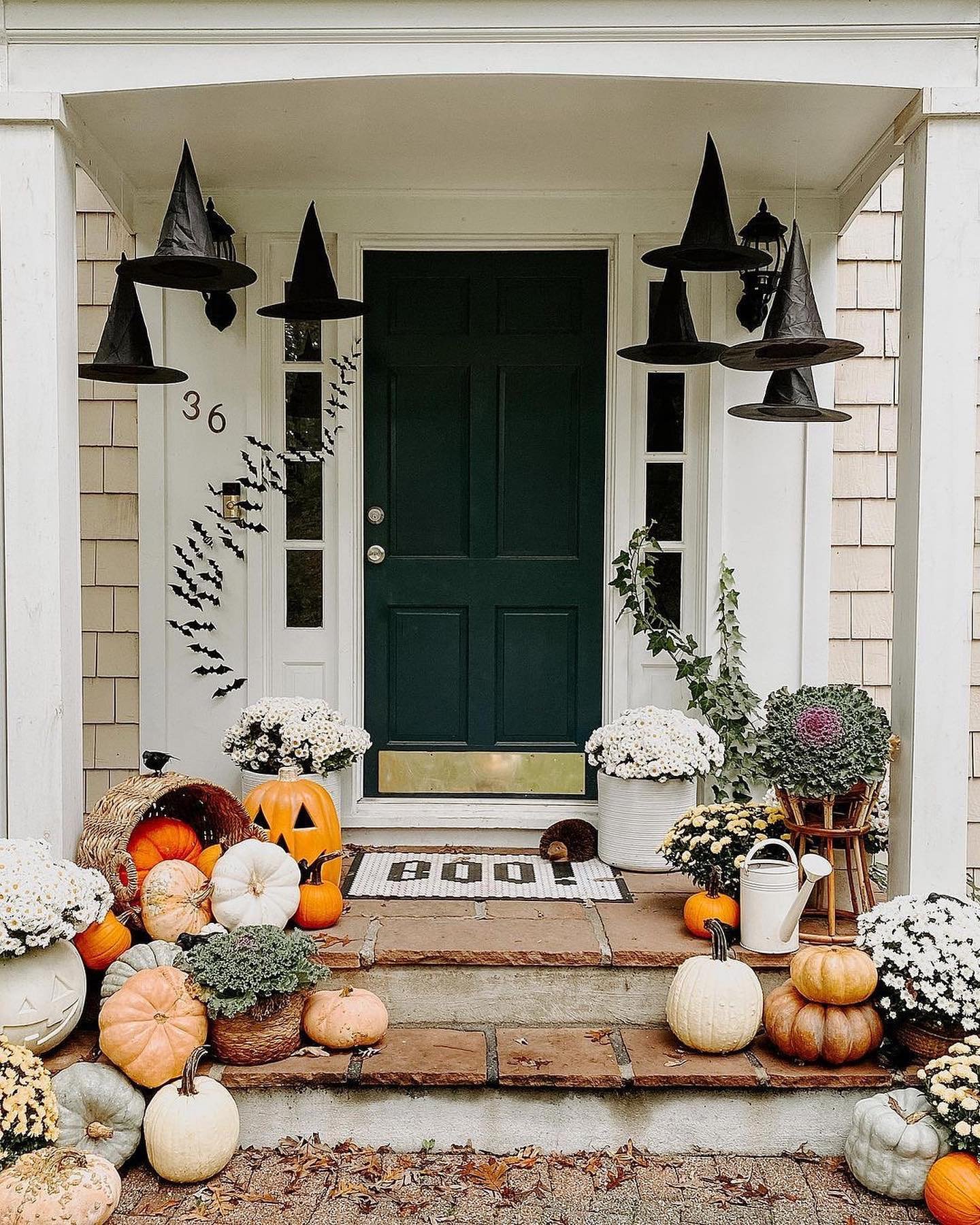 A Halloween porch decorated with floating witch hats, black bat decals, and an assortment of pumpkins and white mums on the steps.