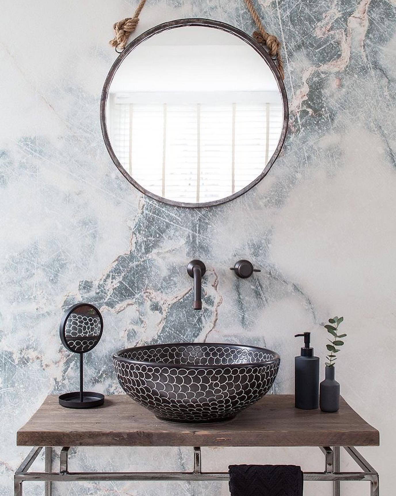 A bathroom featuring a black, patterned vessel sink on a rustic wooden vanity with a metal base.